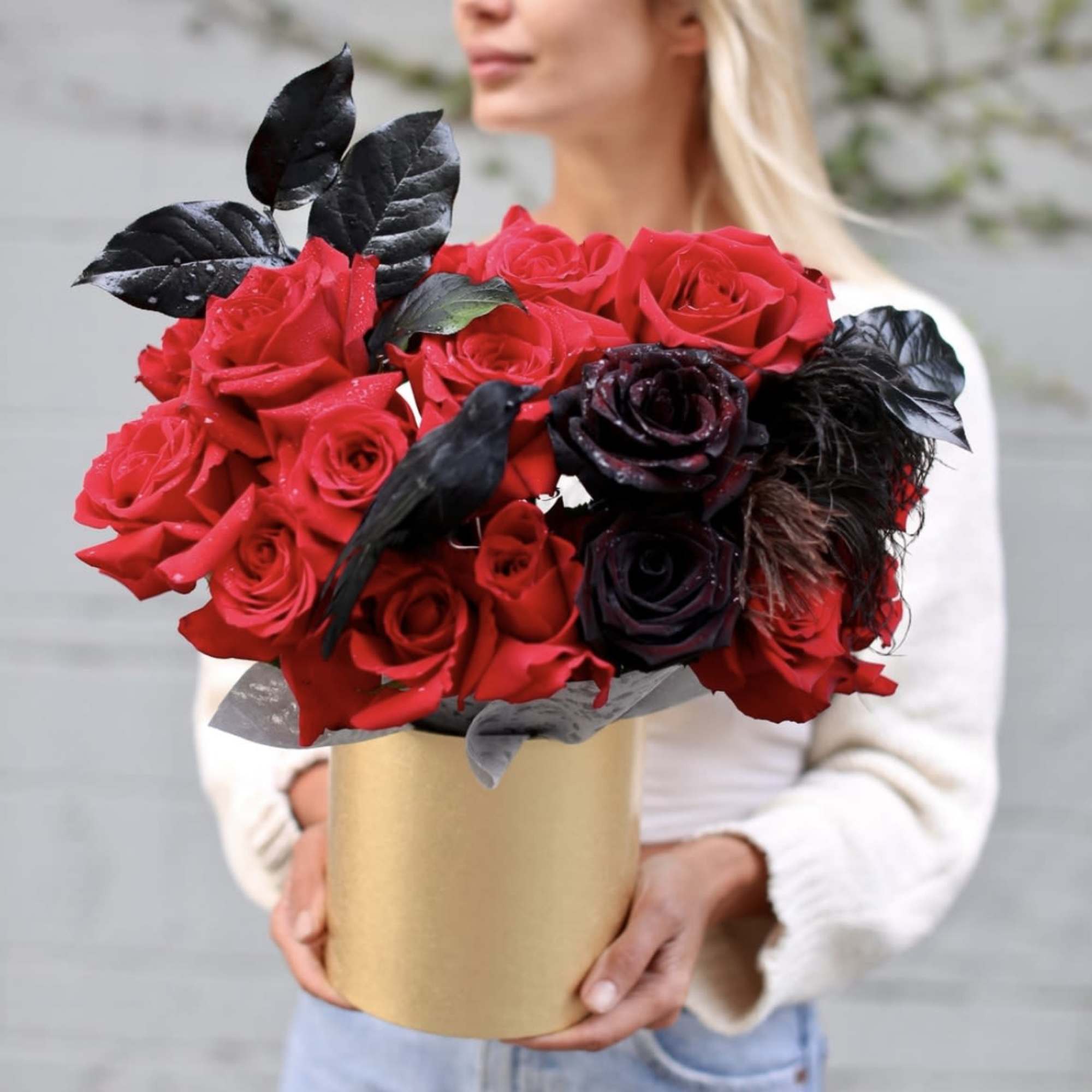 Red and black rose bouquet in a gold box held by a woman