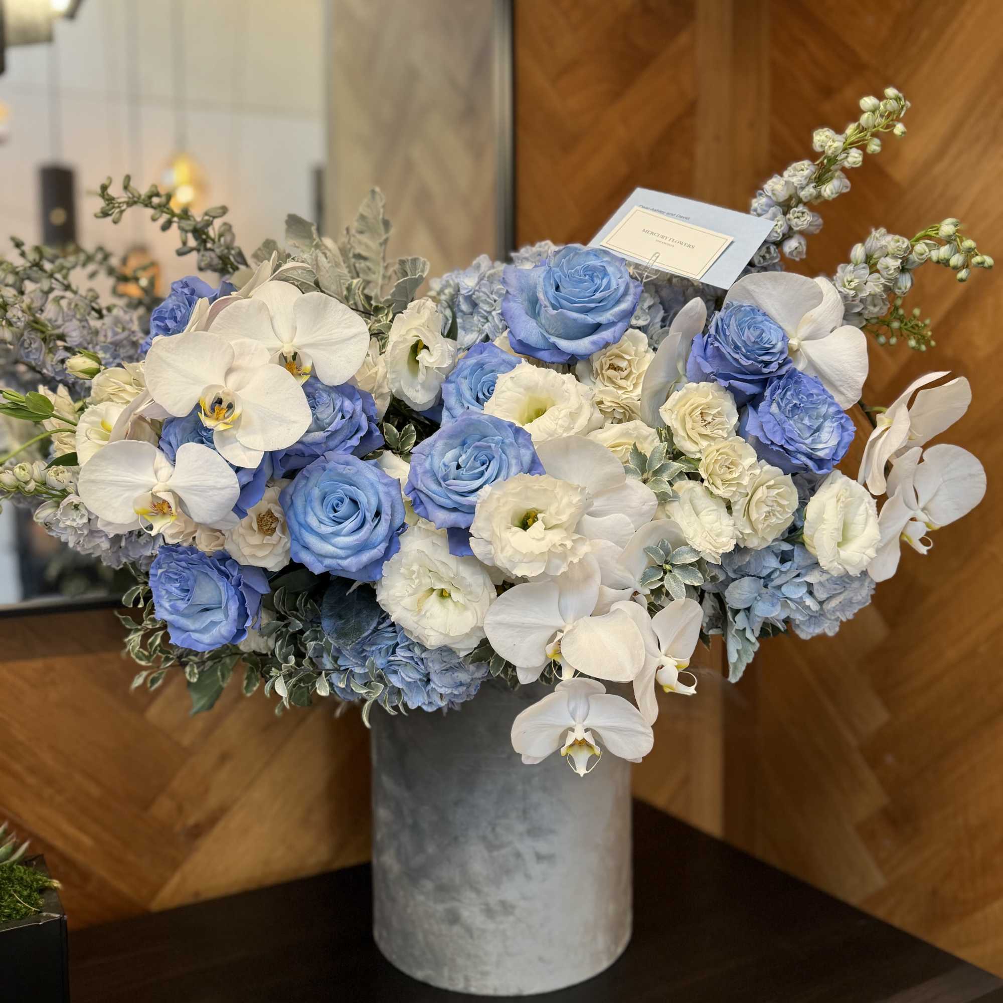 Blue and white floral arrangement in a gray vase with orchids and roses