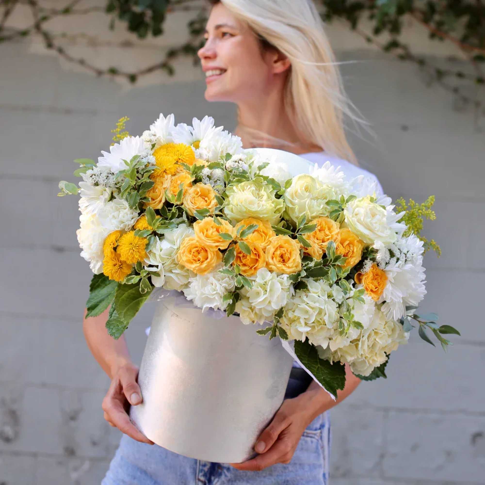 Woman holding a large white hatbox filled with yellow and white flowers
