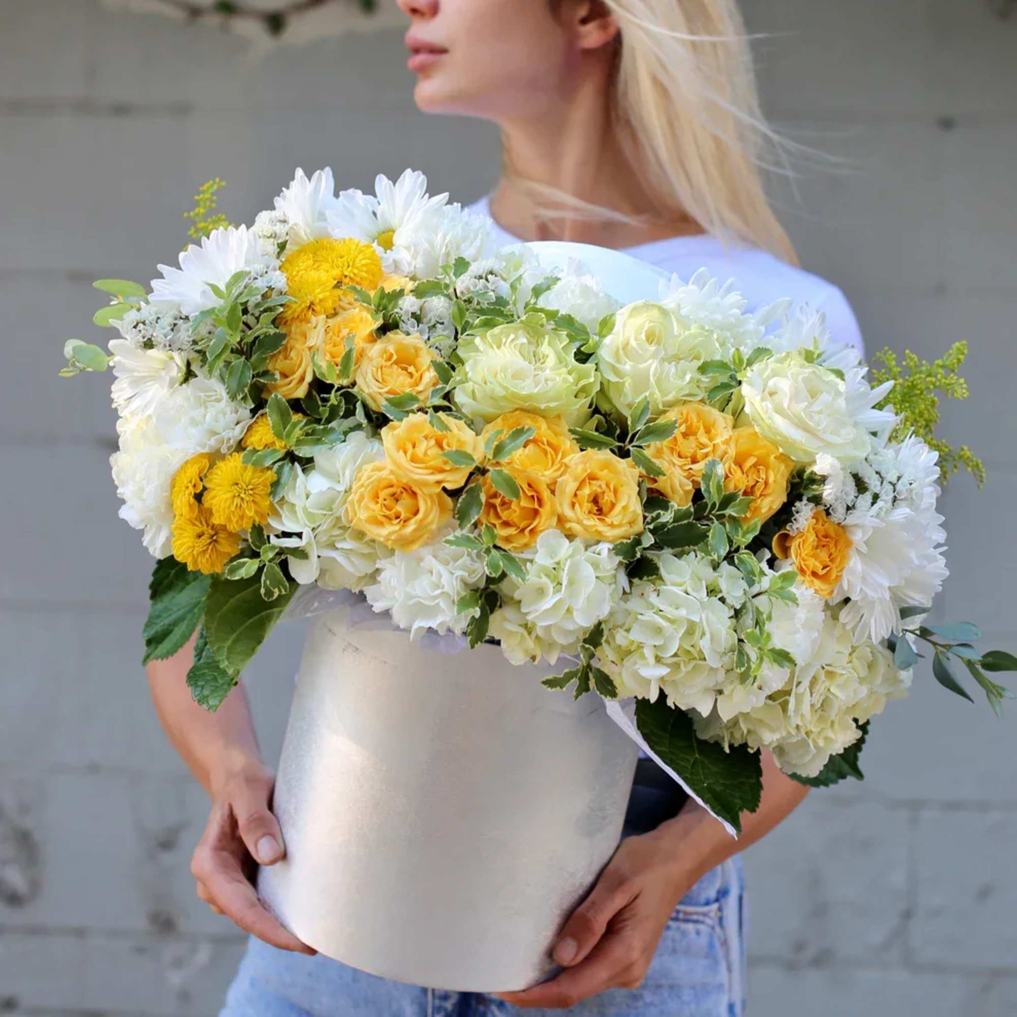 Woman holding a large bouquet of white and yellow flowers in a white box