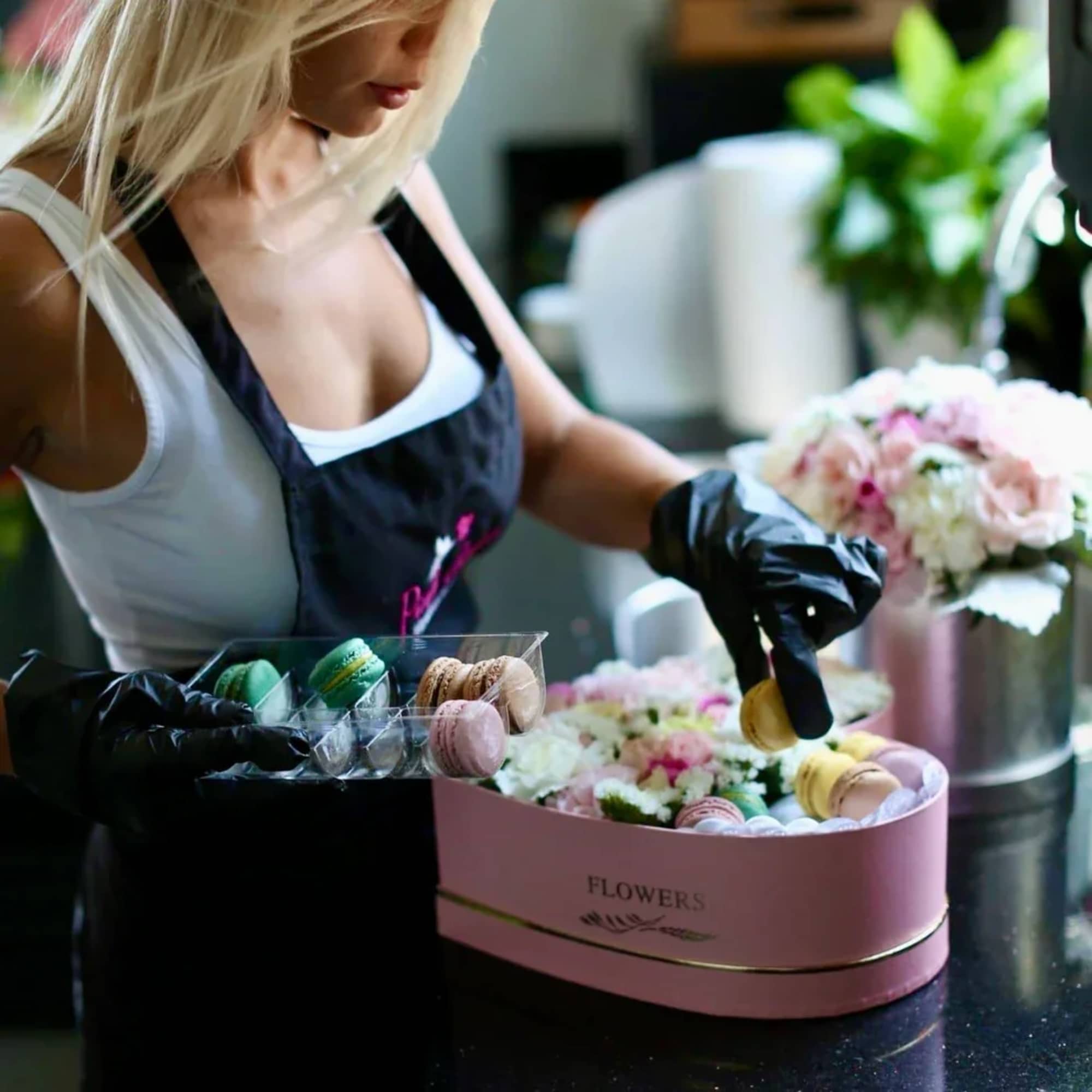 Woman arranging flowers and macarons in a pink gift box