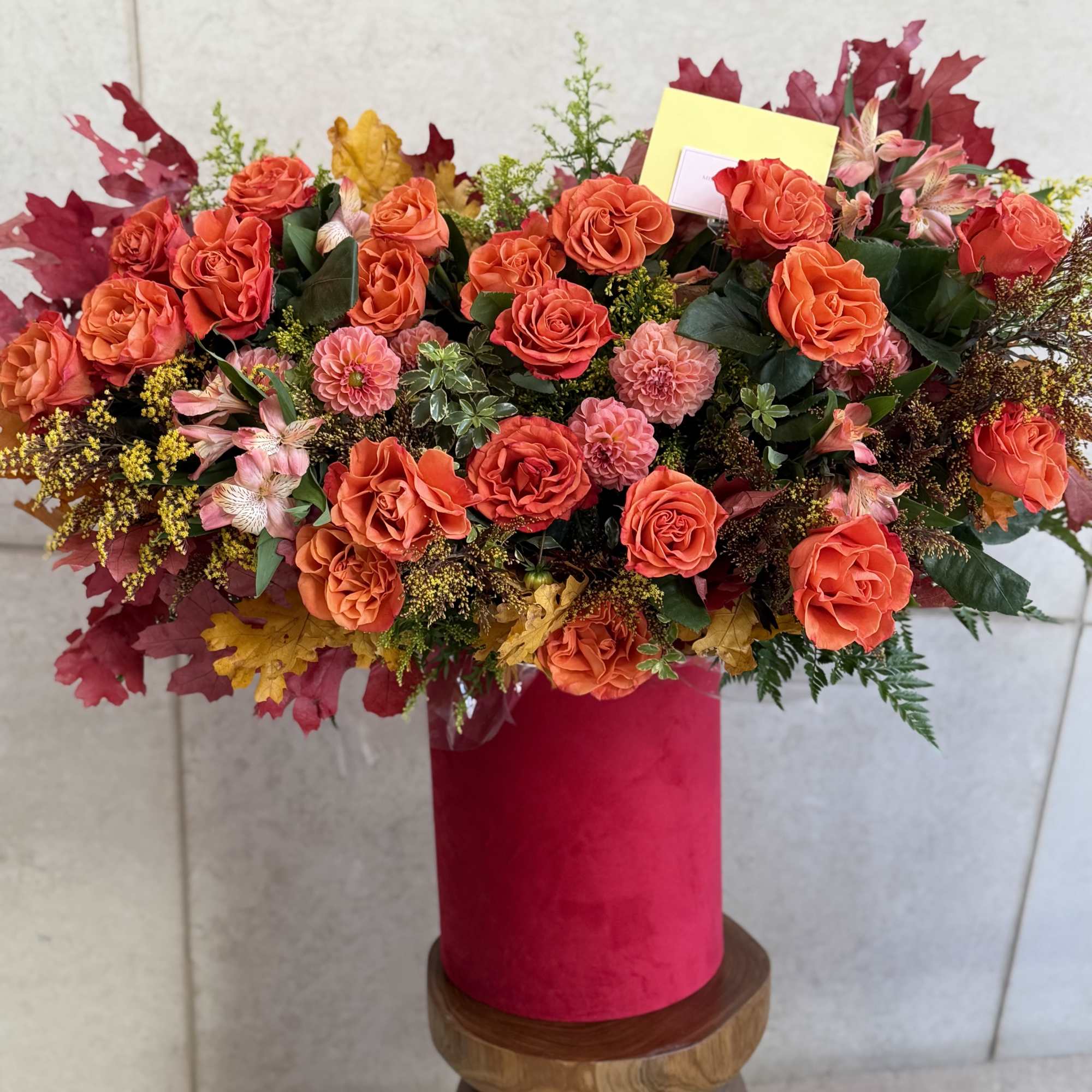 Orange rose arrangement in a pink cylindrical vase with autumn leaves