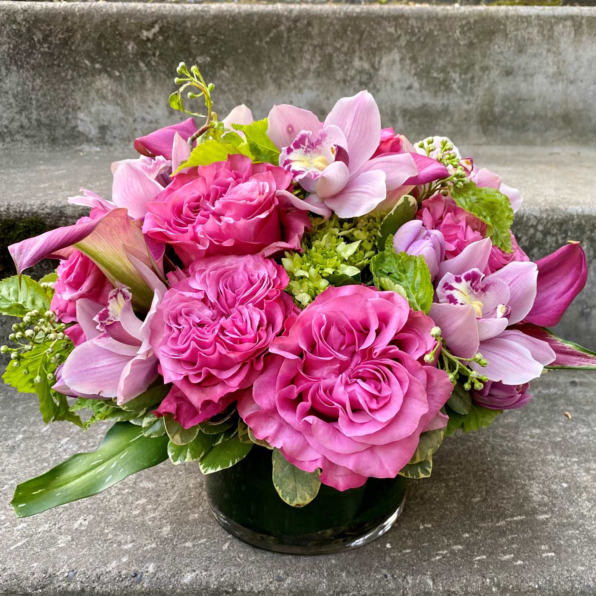 Pink rose and orchid bouquet in a dark glass vase
