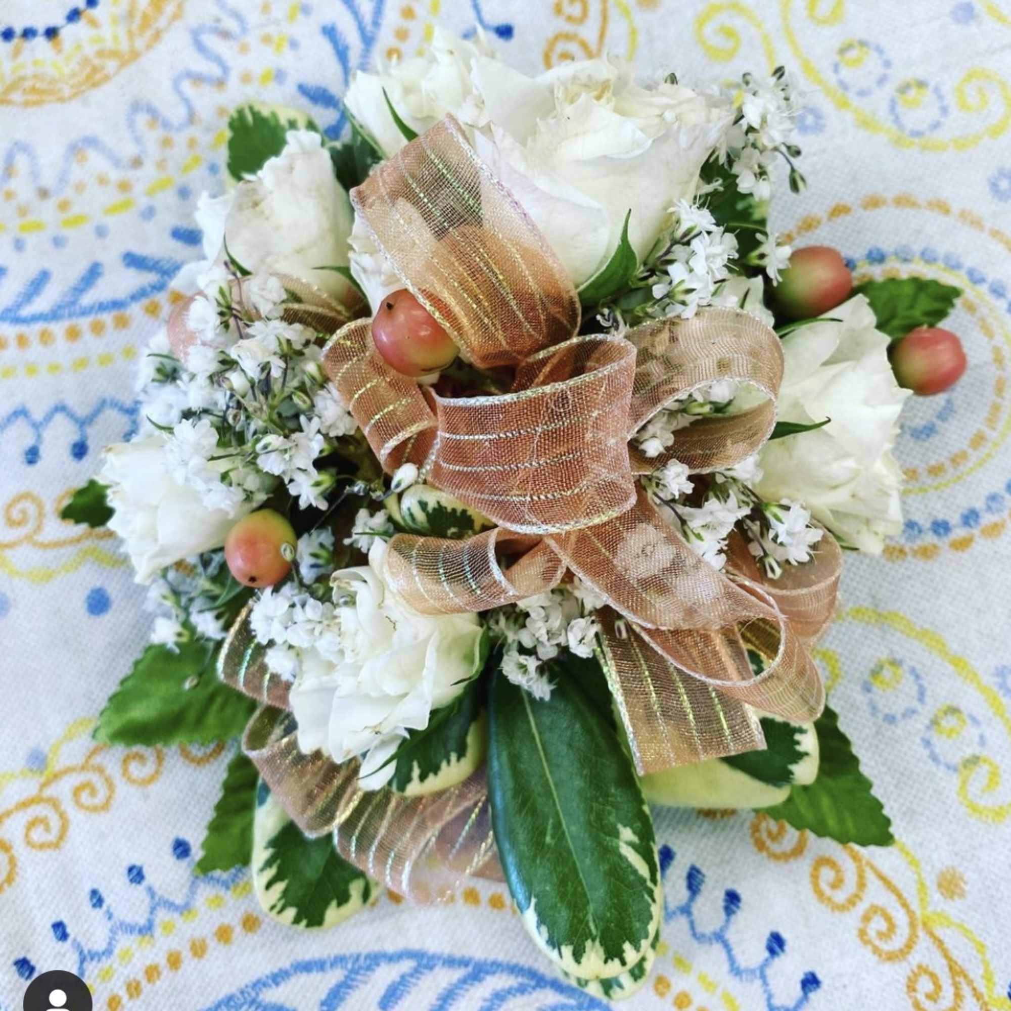 Compact white rose corsage with peach ribbon, white filler flowers, and berries on variegated foliage.