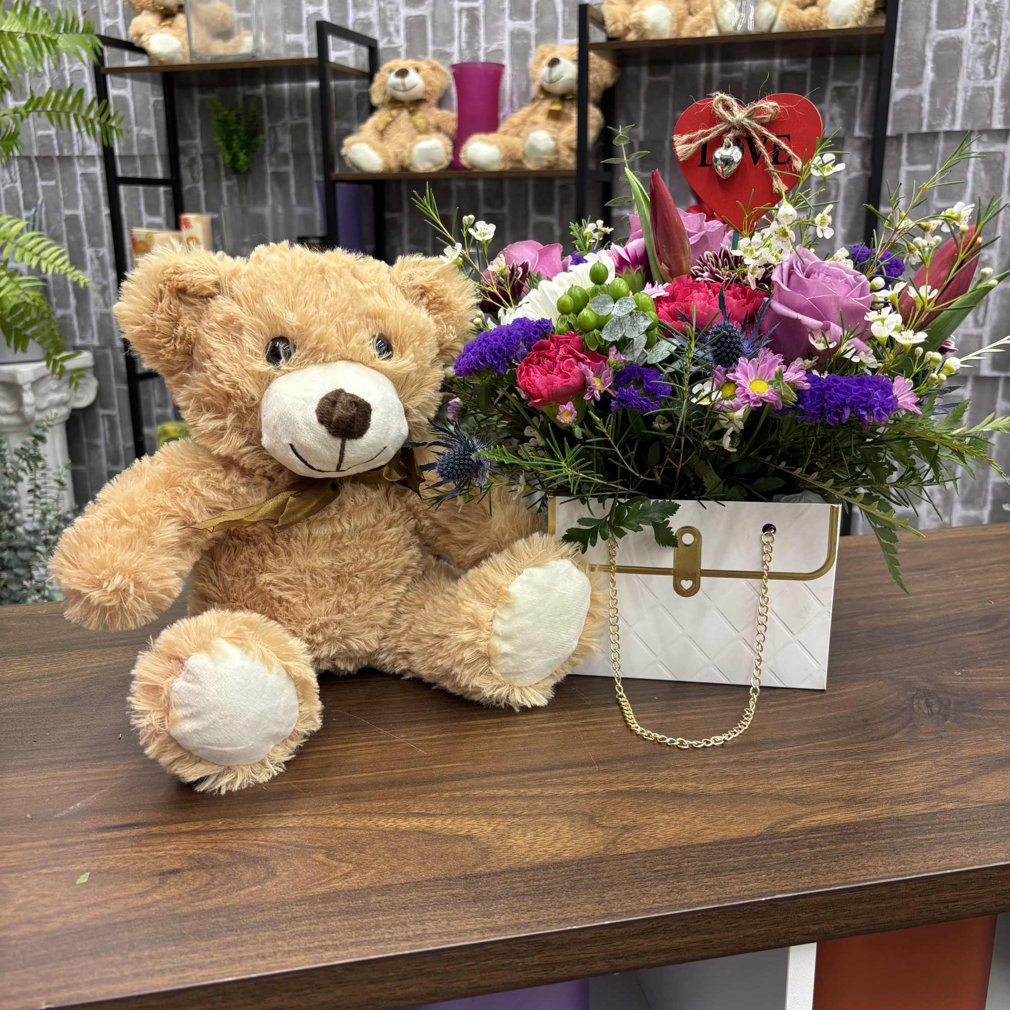 Teddy bear beside a mixed flower arrangement in a gift box