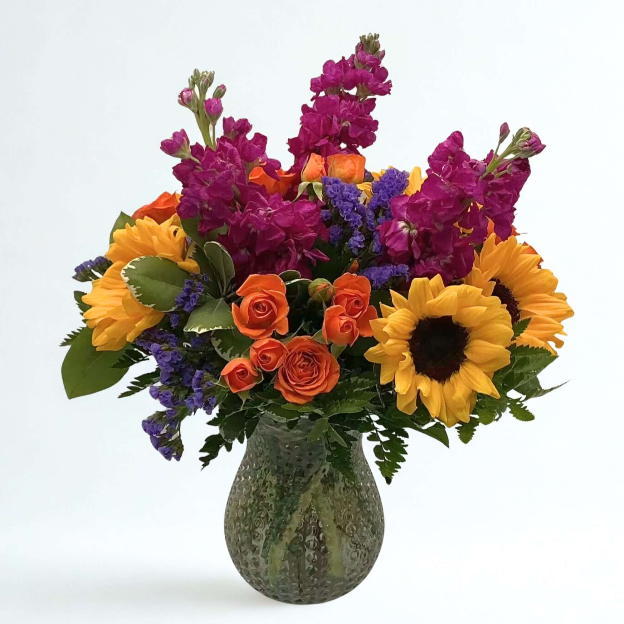 Bouquet of sunflowers, orange roses, and purple flowers in a glass vase