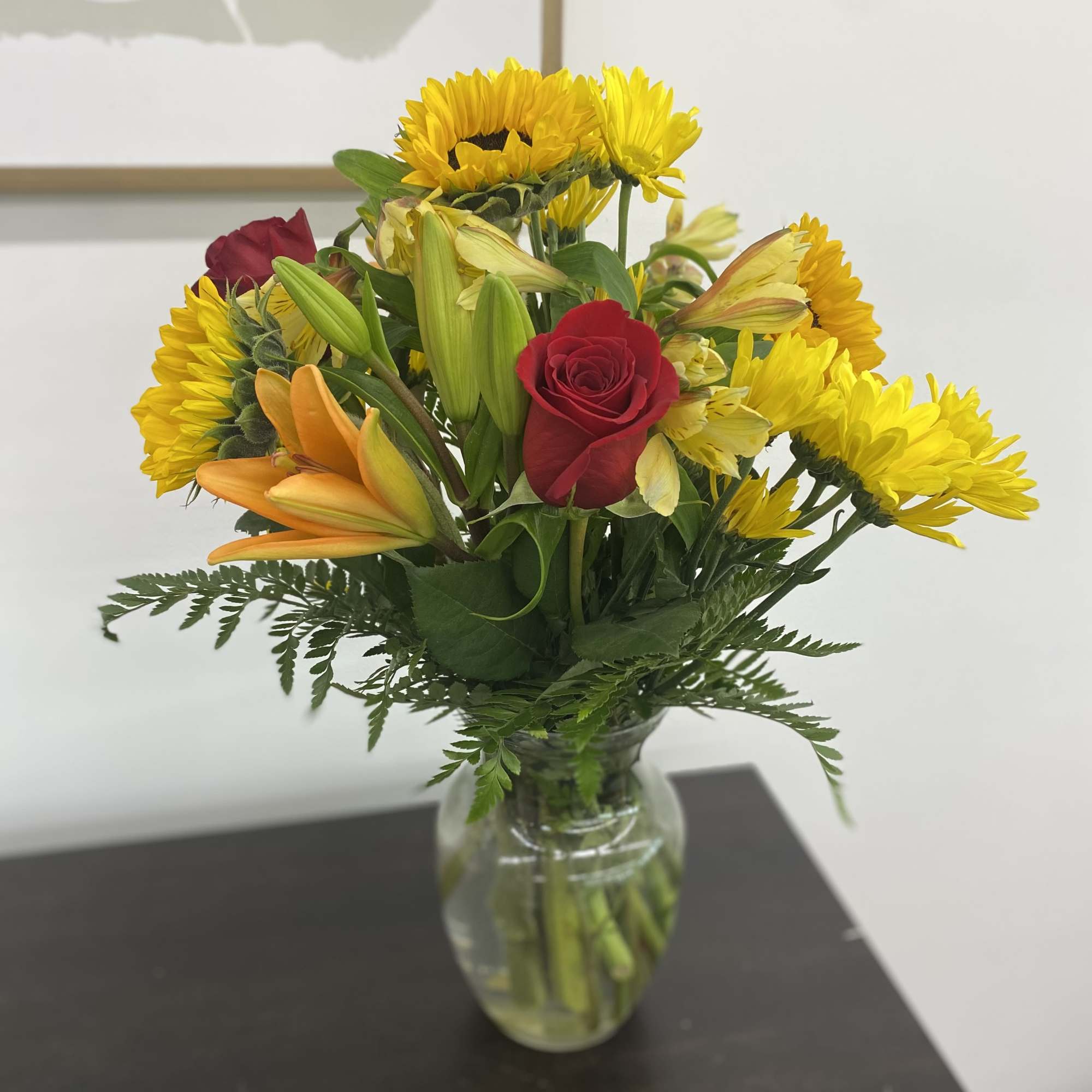 Mixed bouquet of yellow daisies, red roses, and orange lilies in a glass vase