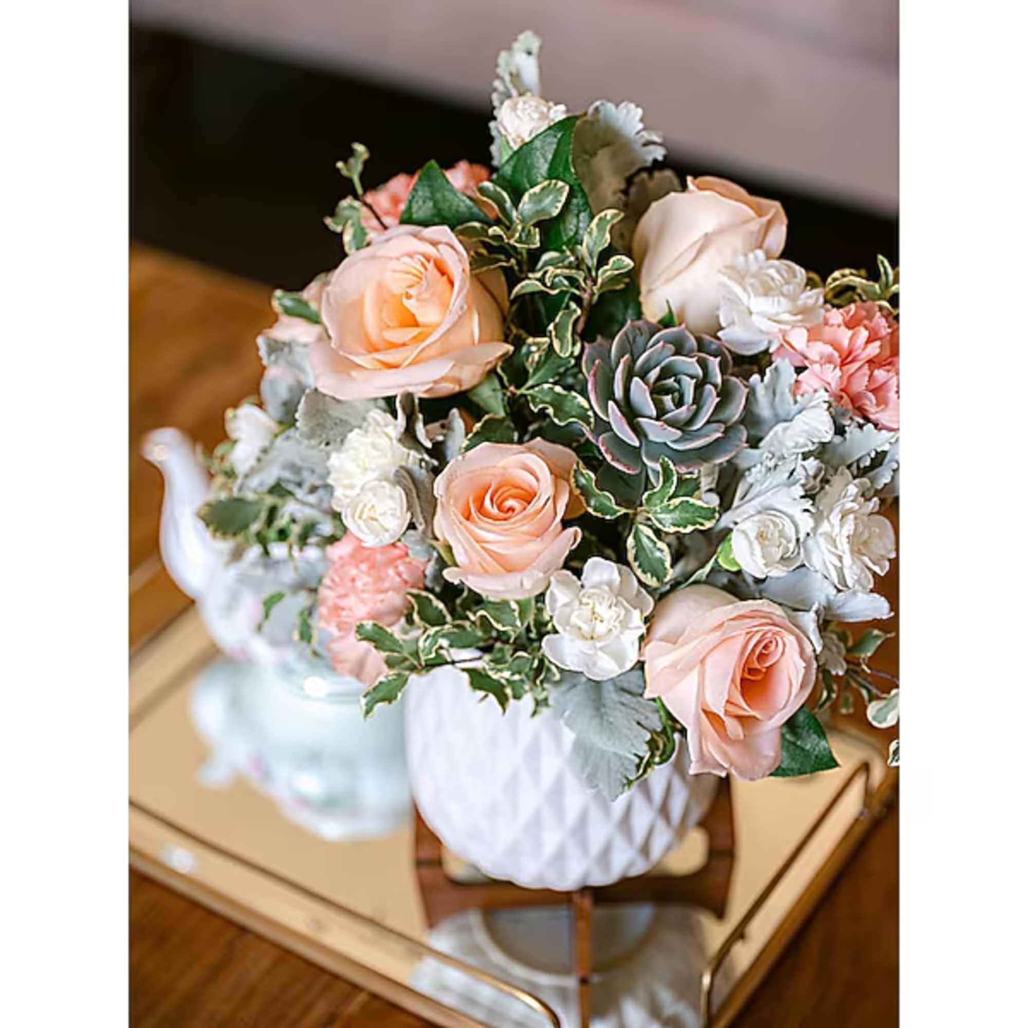Peach roses and white flowers in a white vase with succulent accents