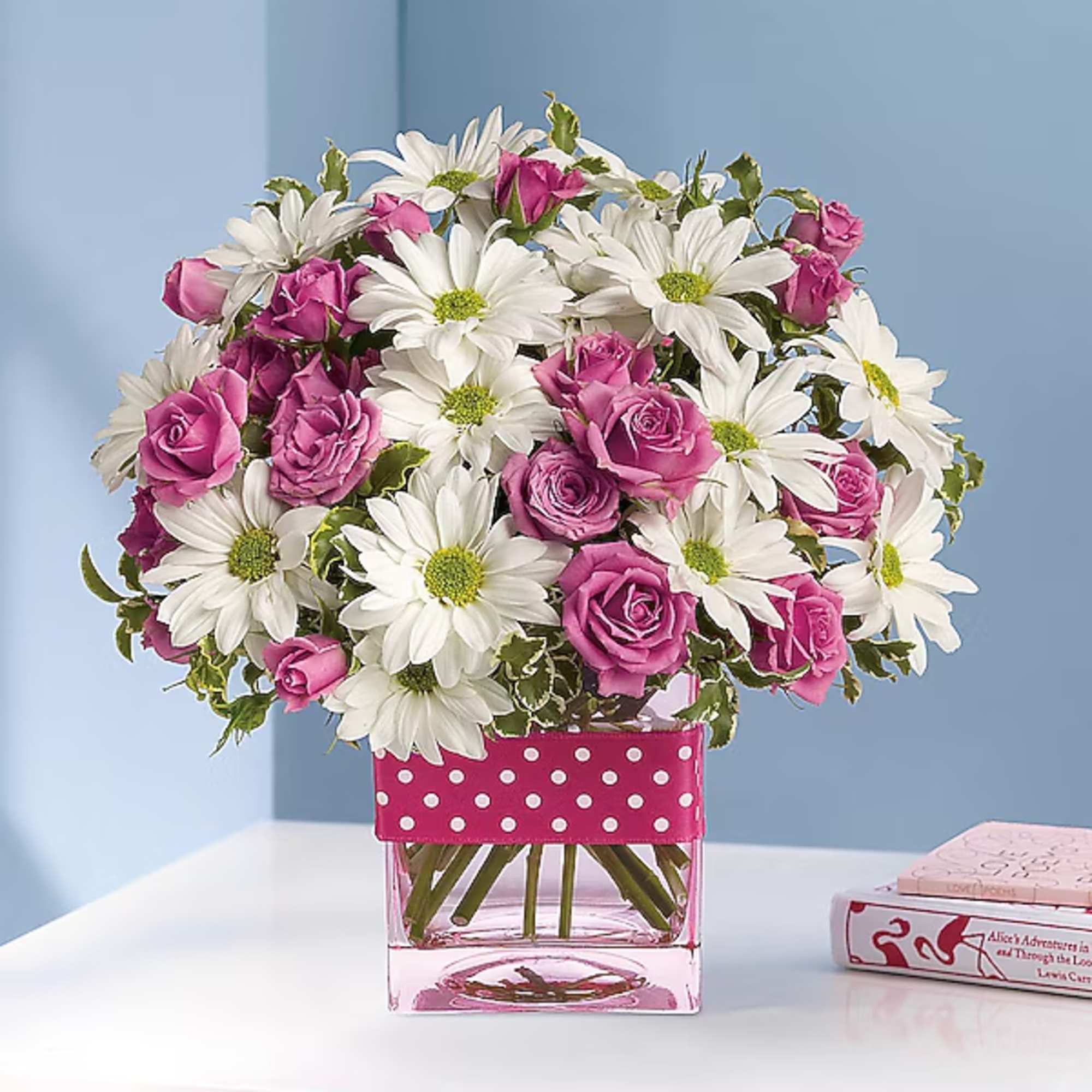 Pink roses and white daisies in a clear square vase with a polka-dot ribbon