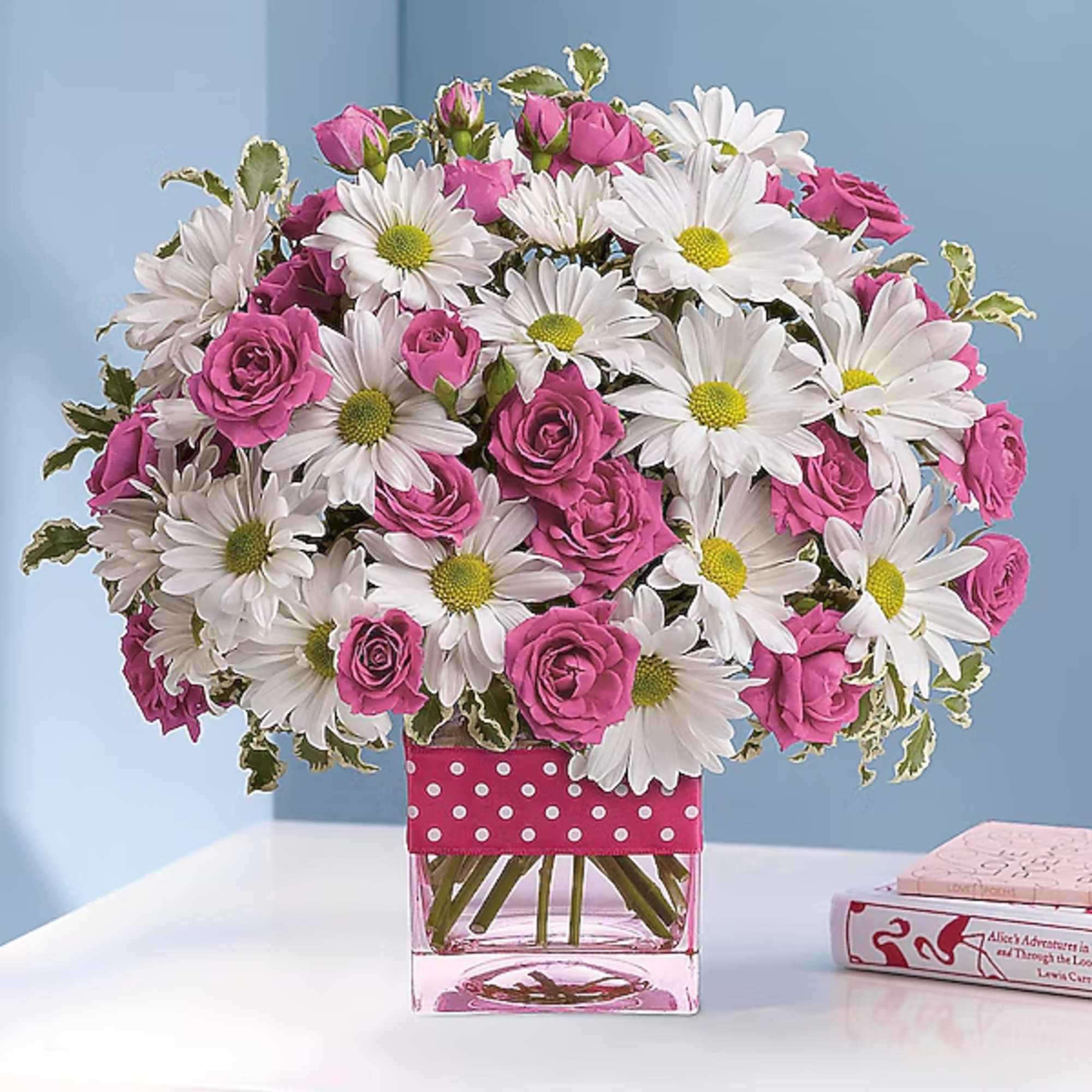 Pink roses and white daisies in a clear square vase with a polka-dot ribbon