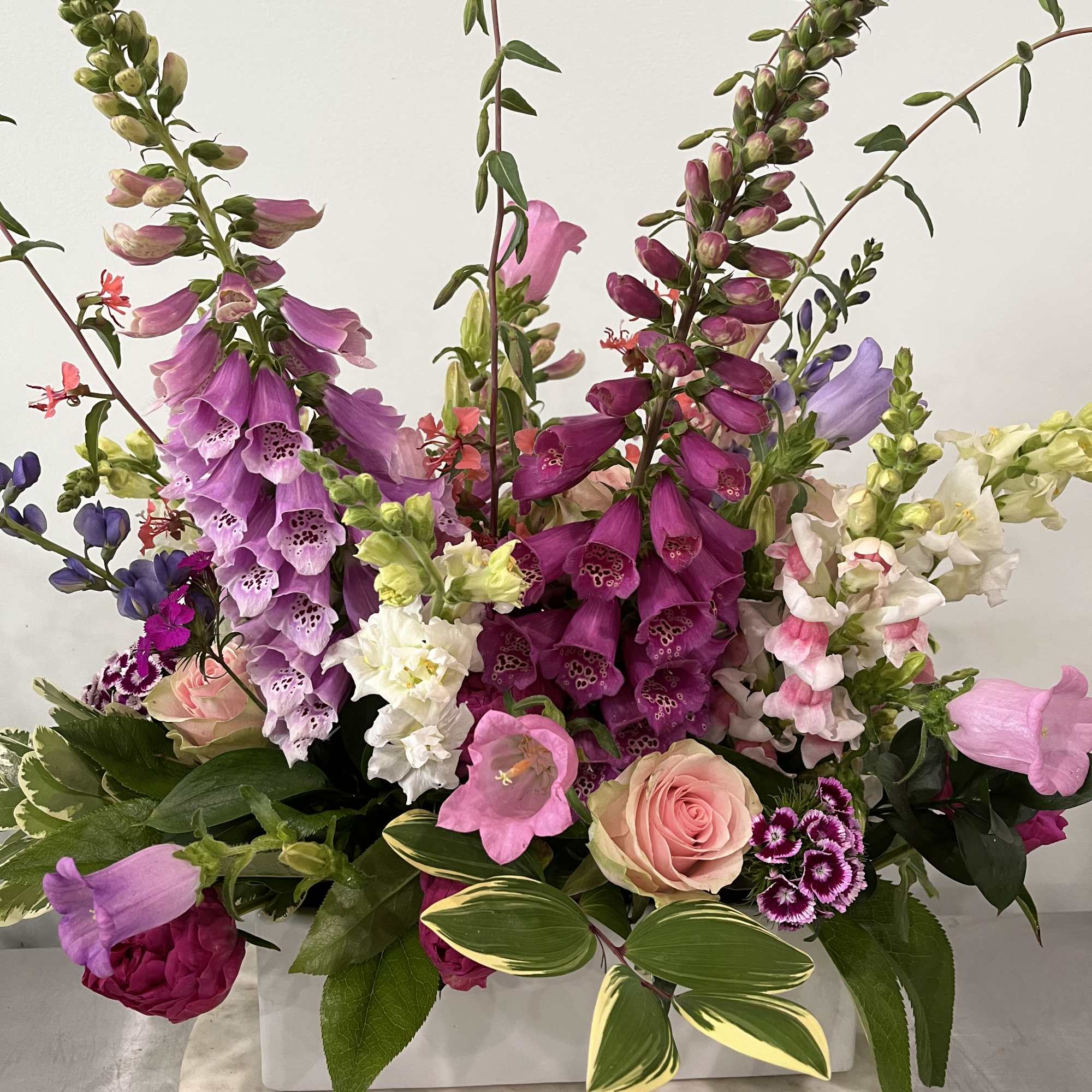 Tall mixed bouquet with pink, purple, and white blooms in a white container.