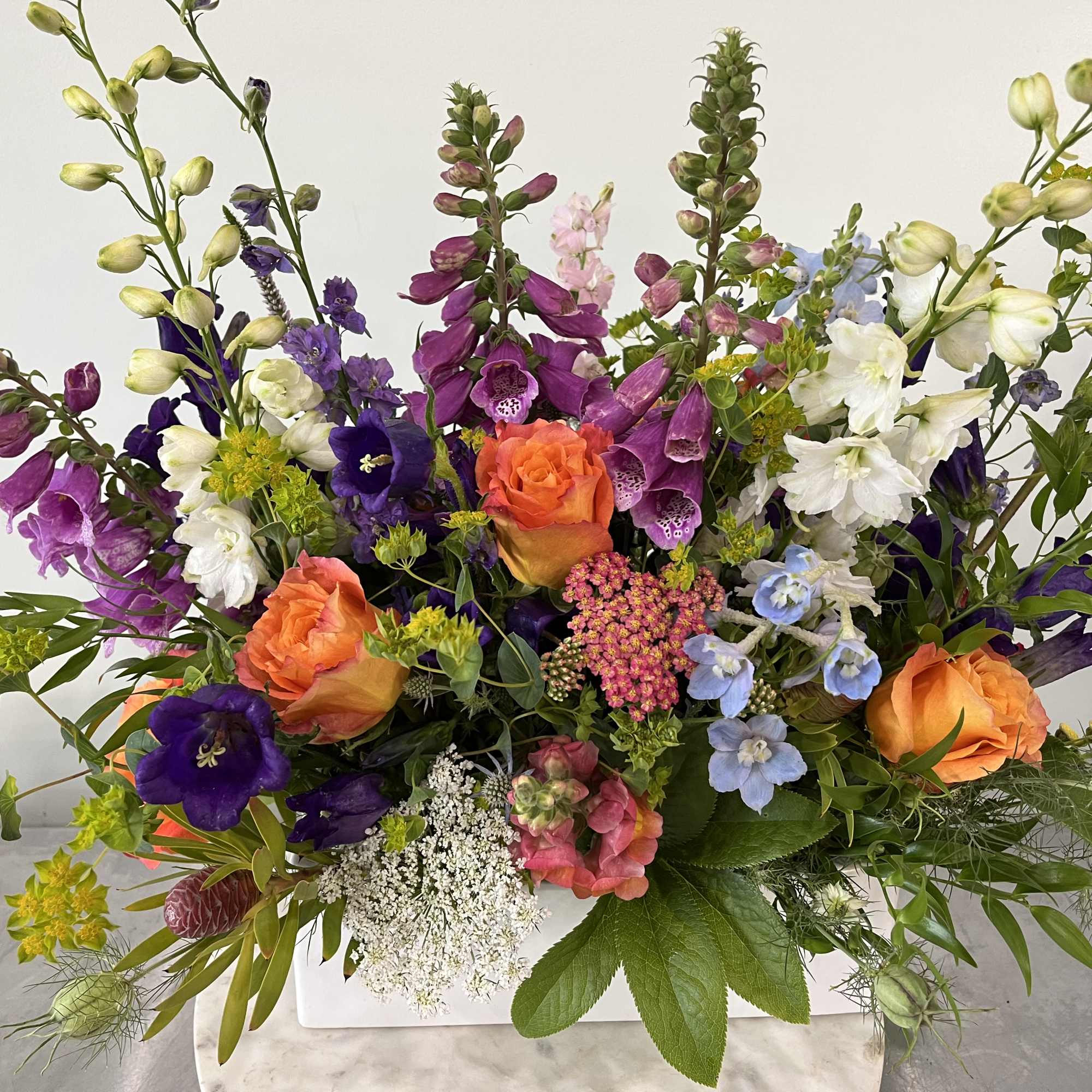Mixed bouquet with orange roses and purple blooms in a white container