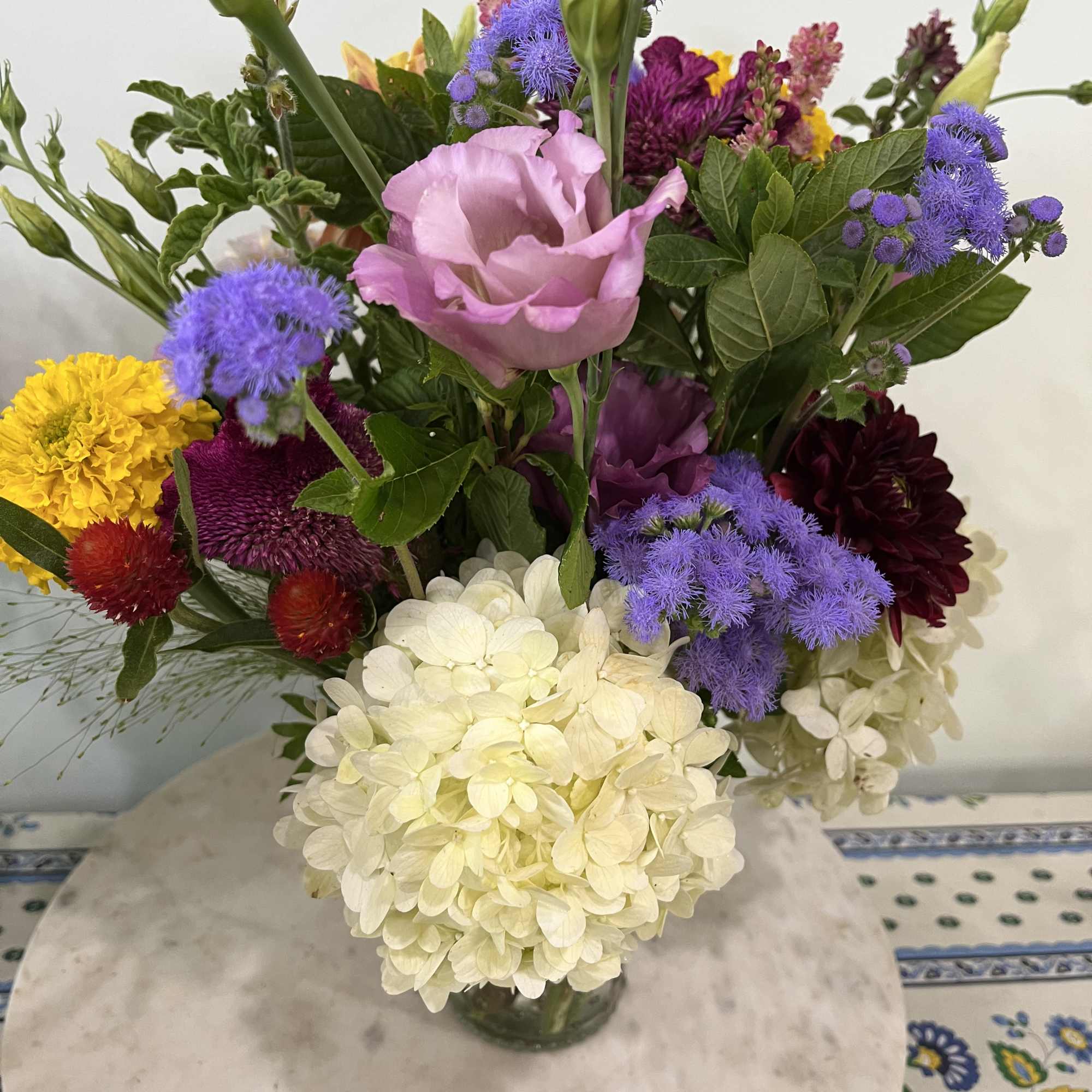 Colorful mixed bouquet with white hydrangeas, pink lisianthus, and bright blooms in a clear glass vase.