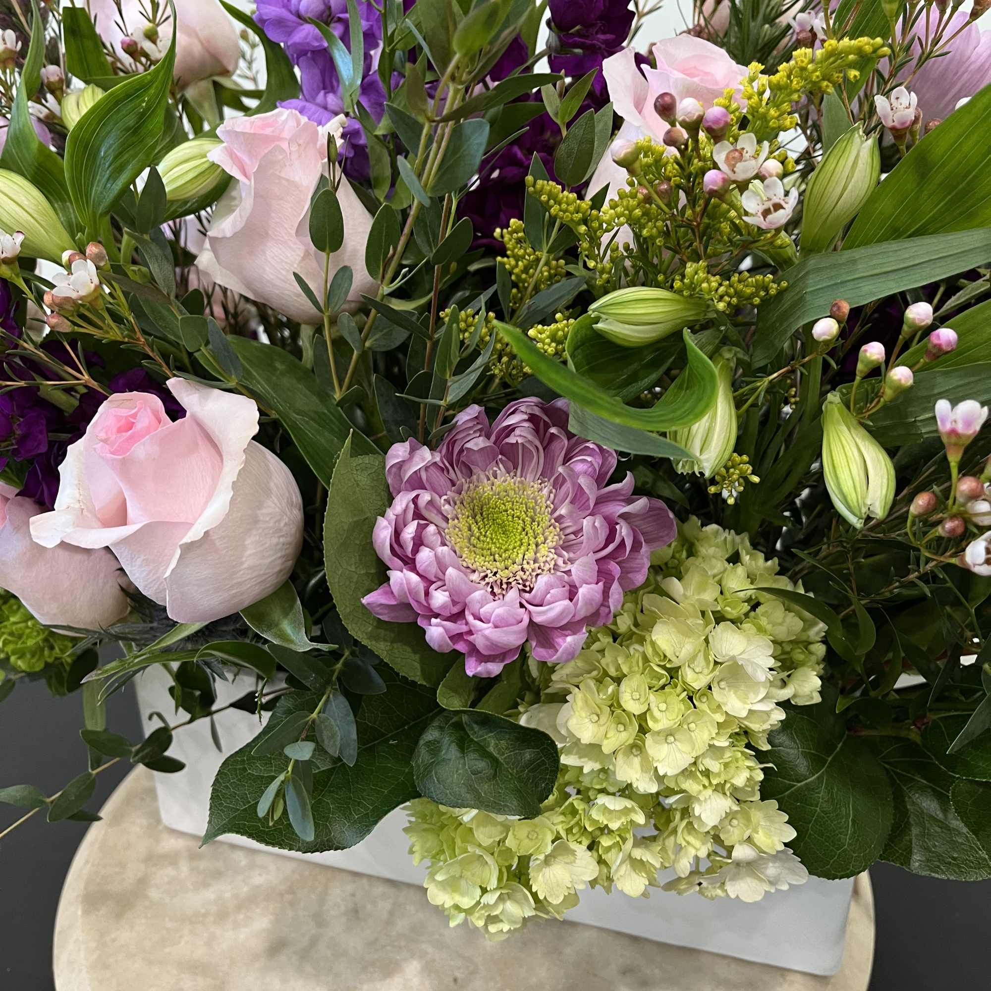 Mixed bouquet with pink roses, purple blooms, and green hydrangea in a white box