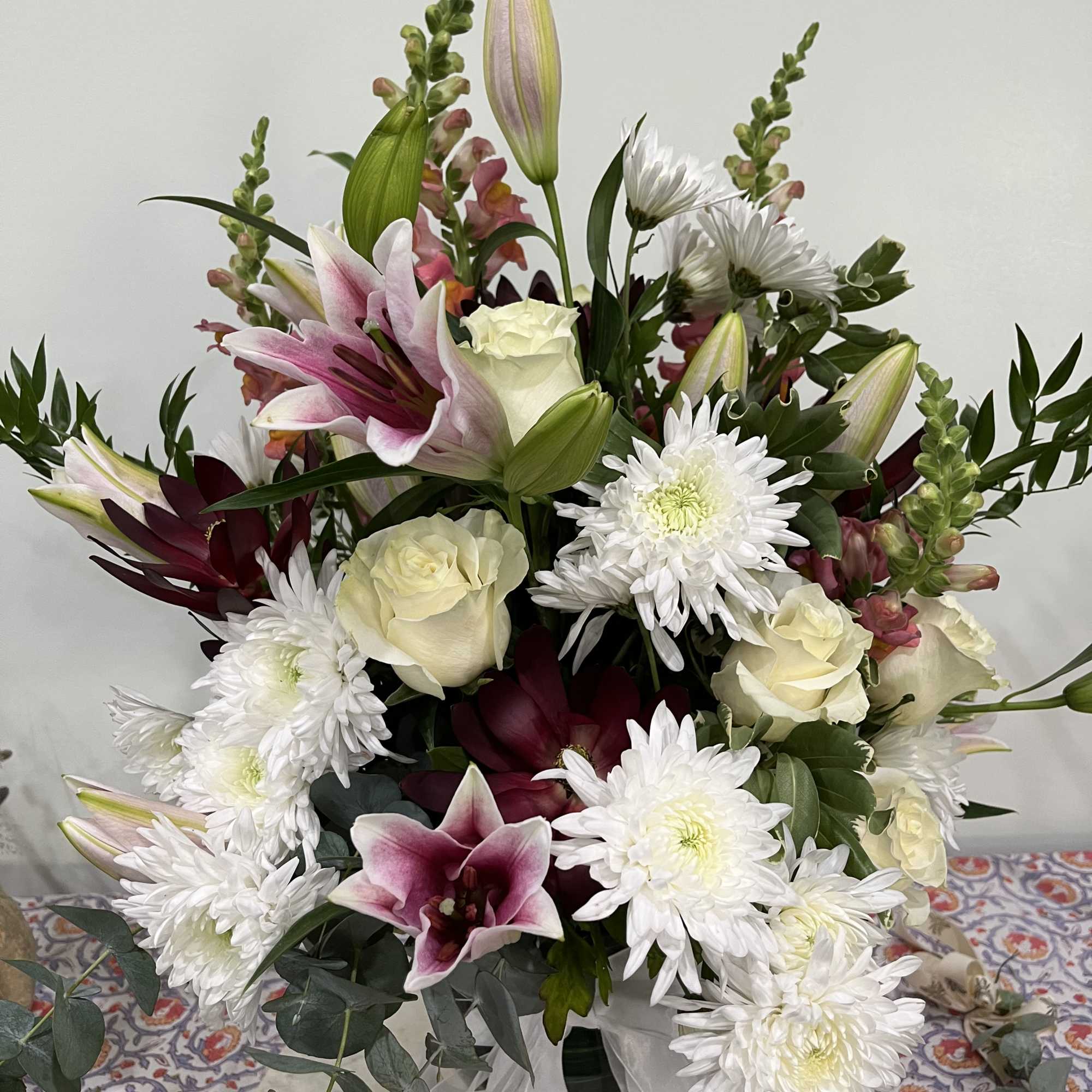 Mixed bouquet with white chrysanthemums, pink lilies, and cream roses in a glass vase