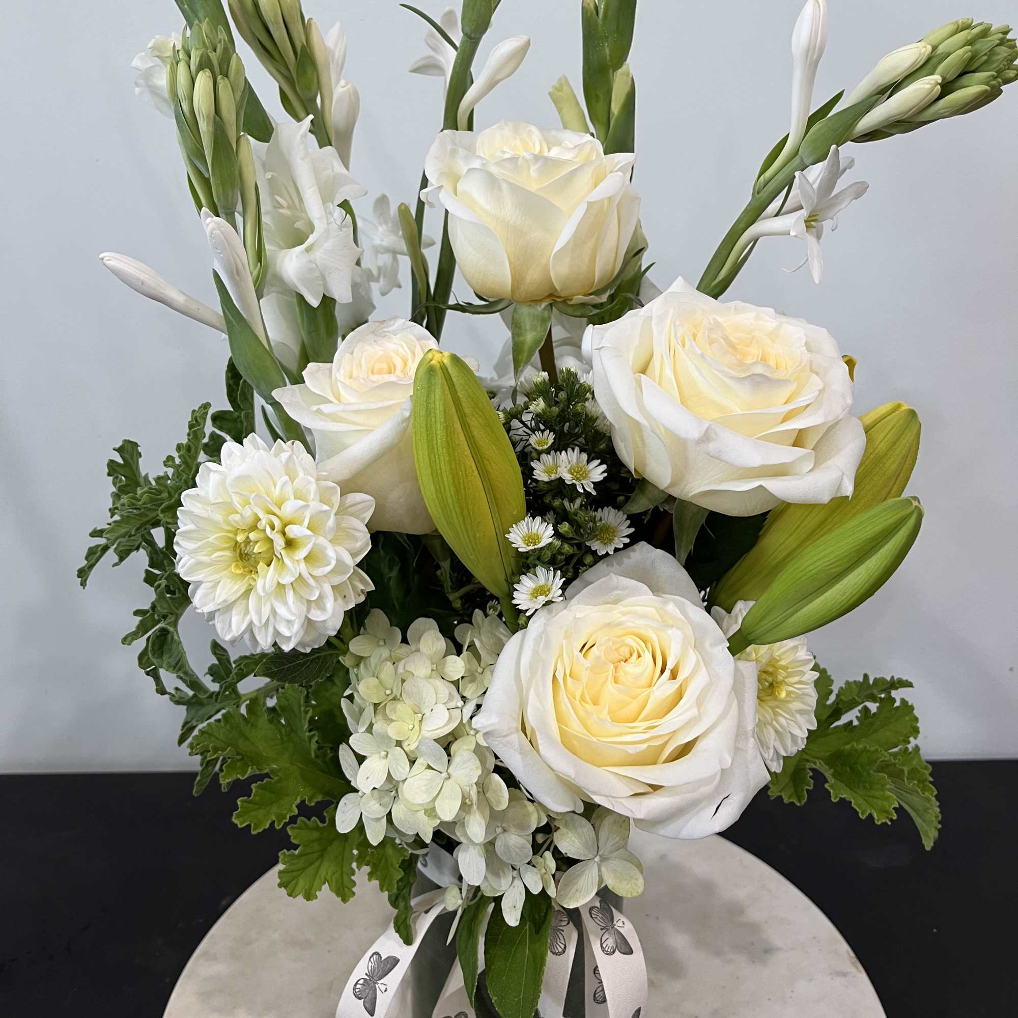 White roses and lilies arranged in a vase with green foliage.