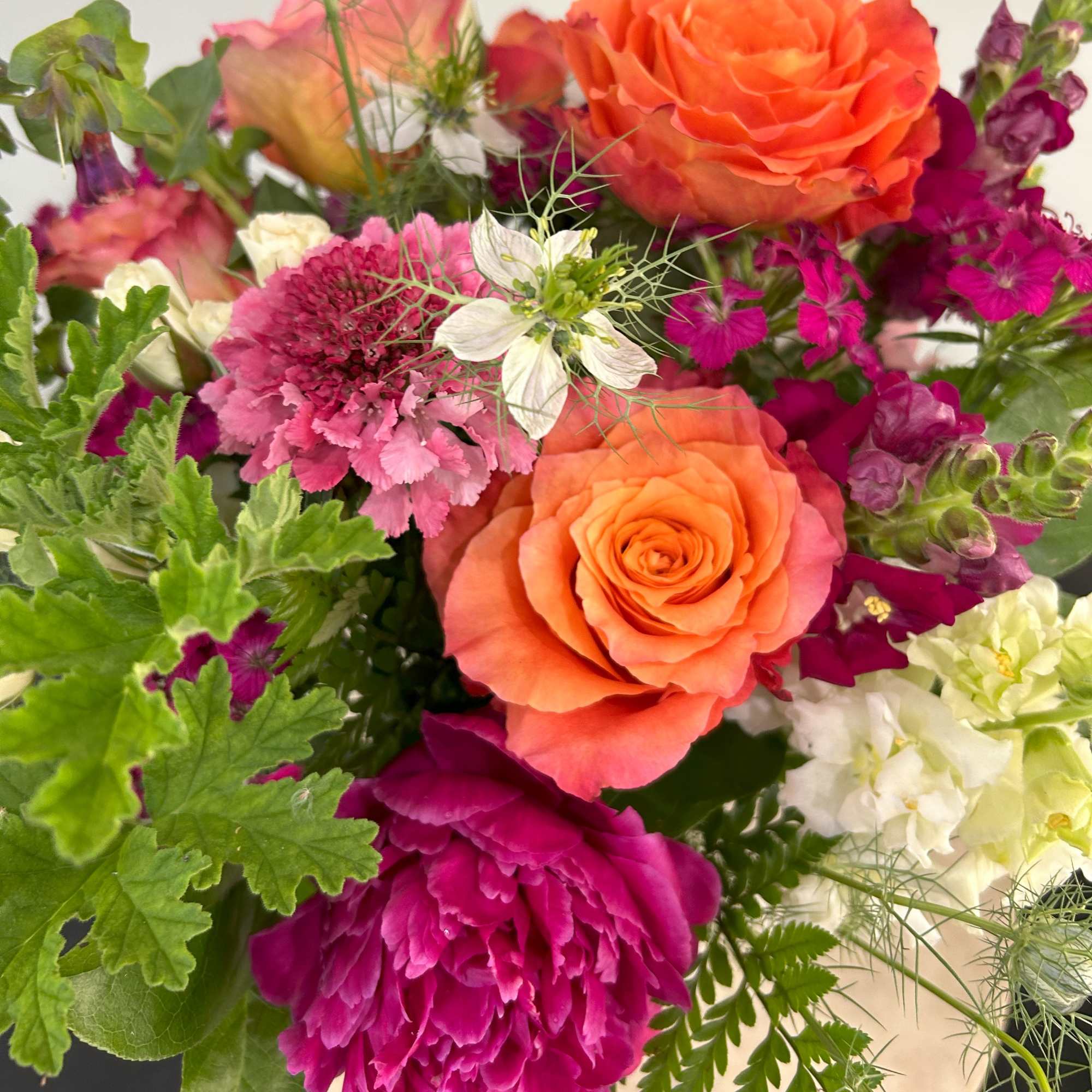 Mixed bouquet of bright orange roses, hot pink blooms, and white flowers in a lush arrangement