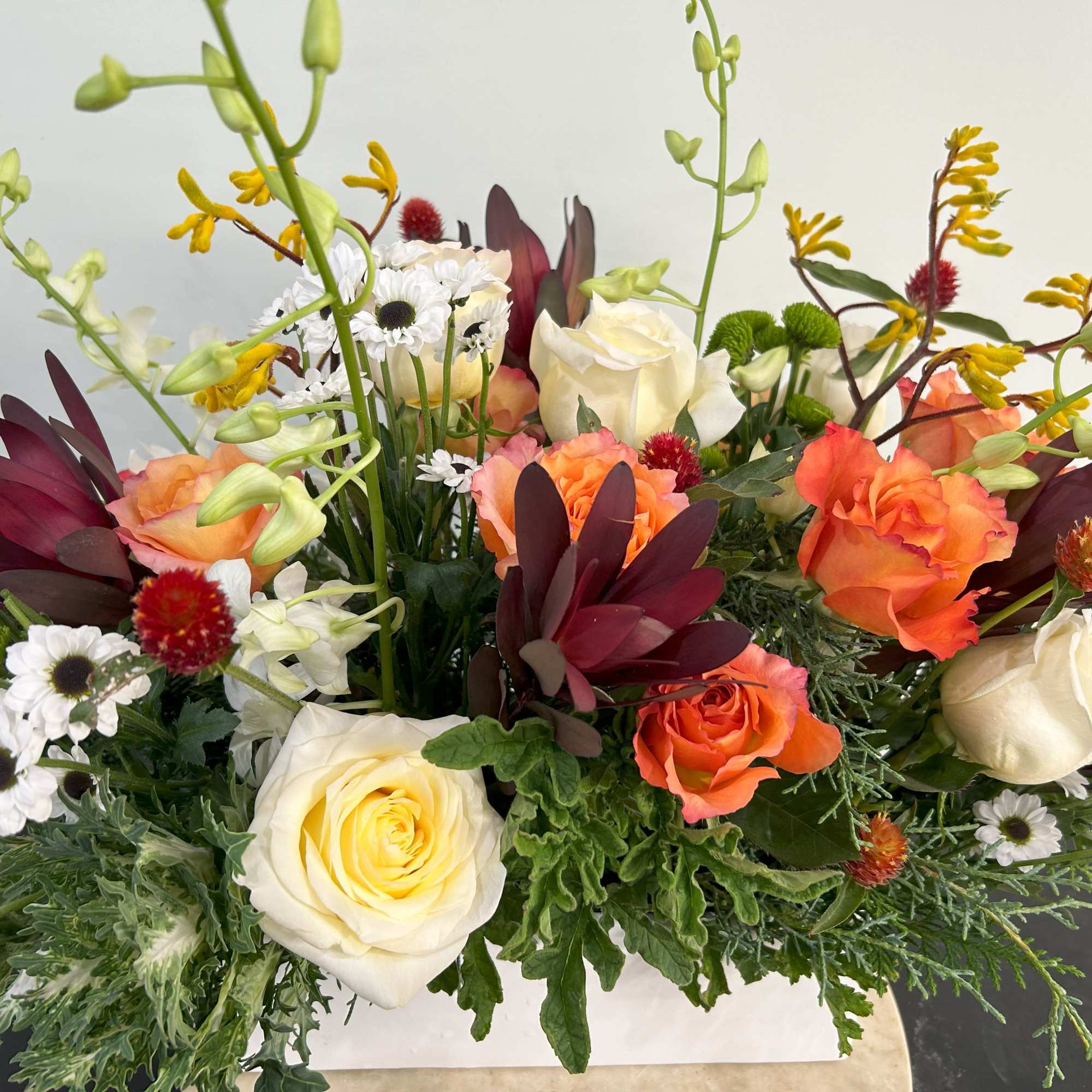 Mixed floral arrangement with cream and orange roses and white daisies