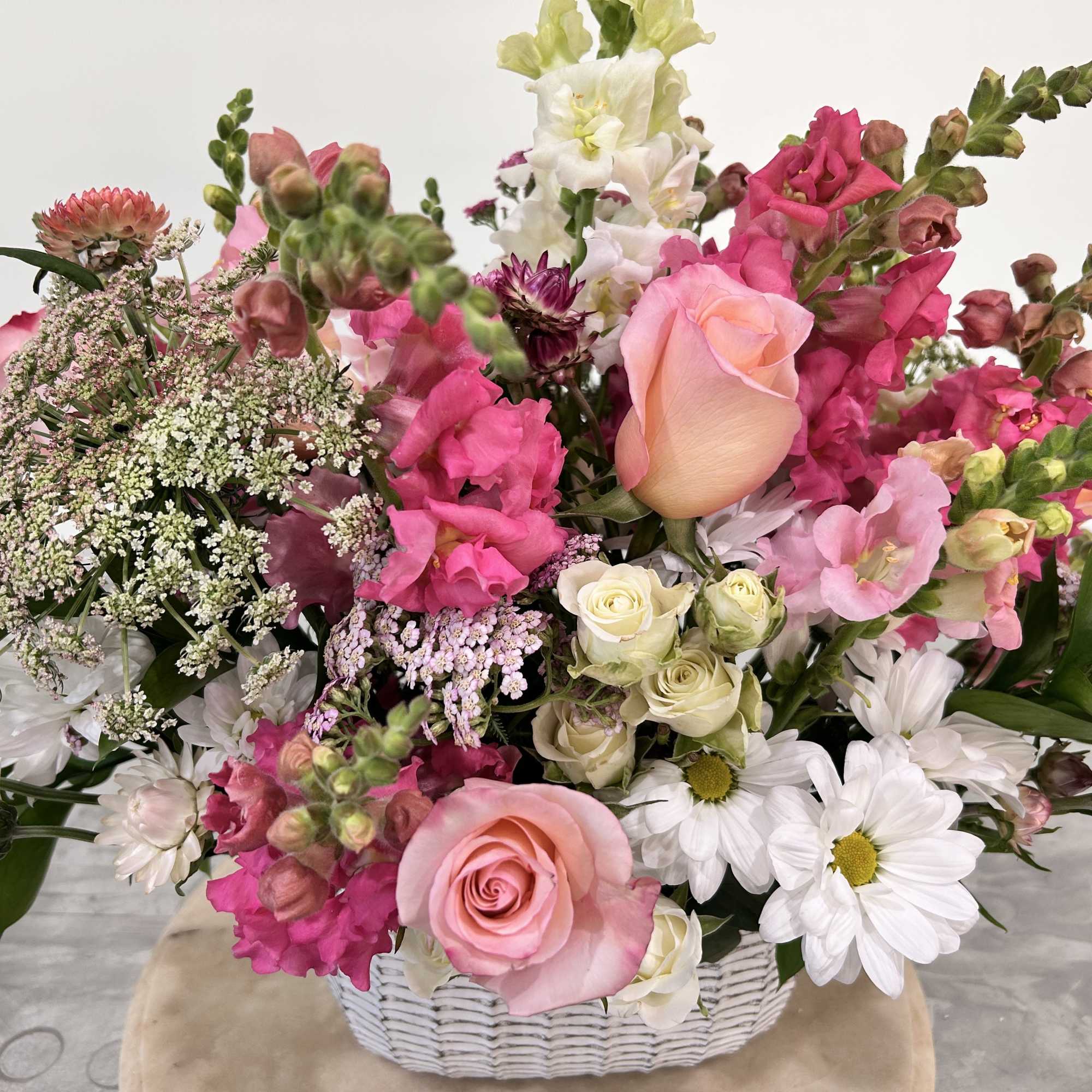 Pink and white mixed flower arrangement in a white basket