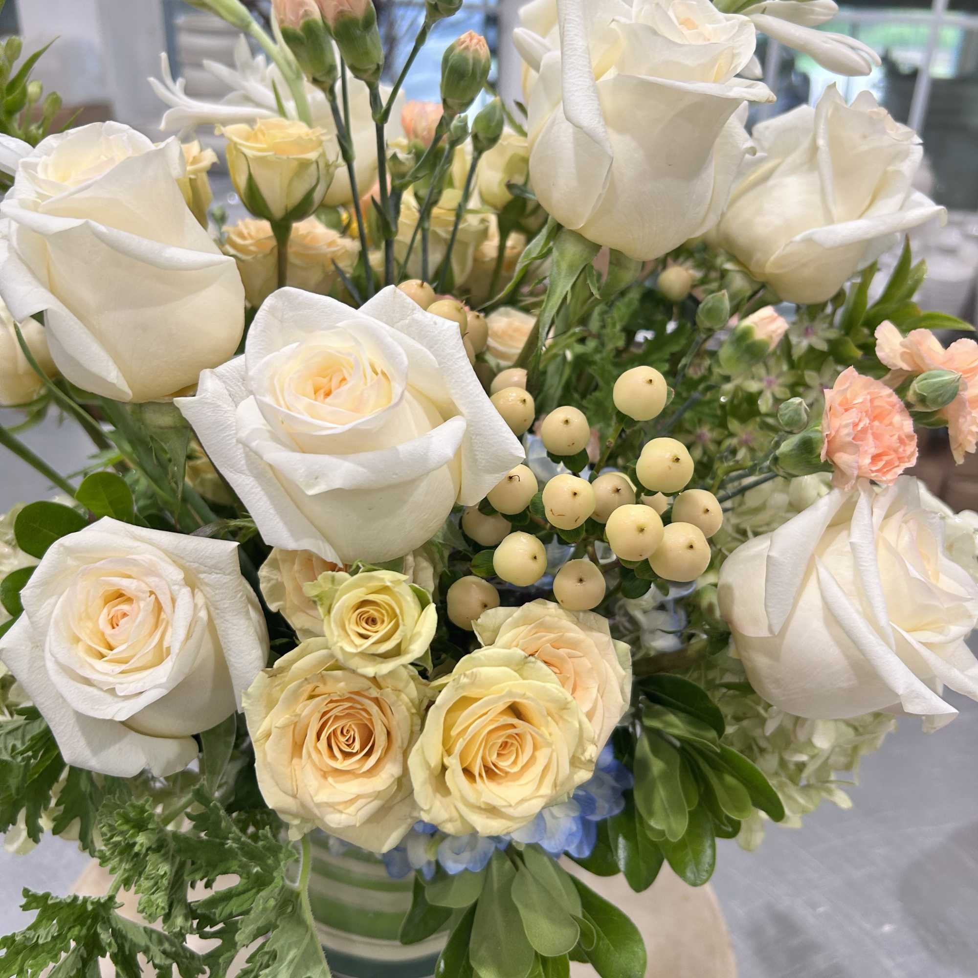 White and pale peach roses arranged in a glass vase with small cream berries.