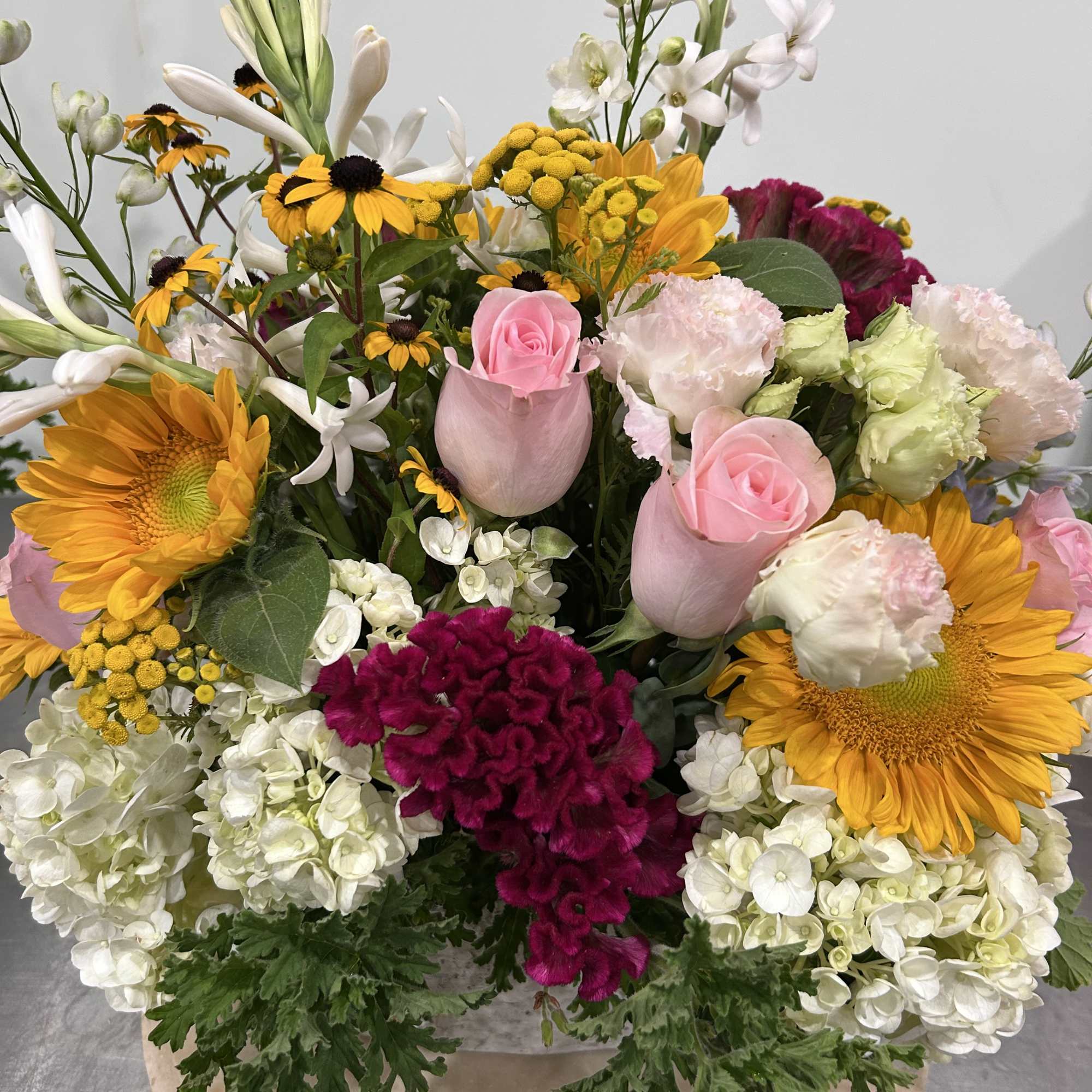 Mixed bouquet with pink roses, sunflowers, and white blooms in a round container