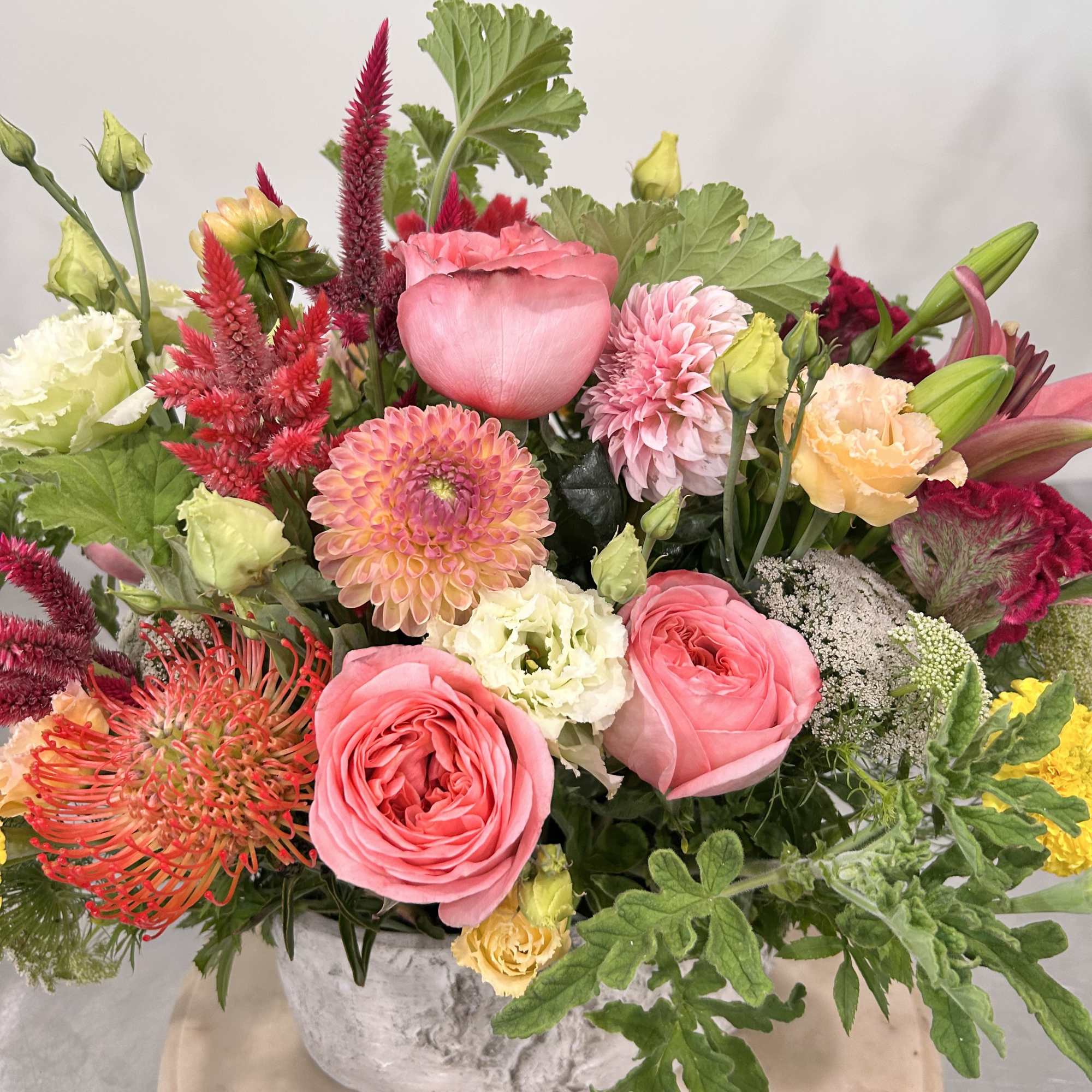 Mixed bouquet of pink, peach, and red flowers in a white vase