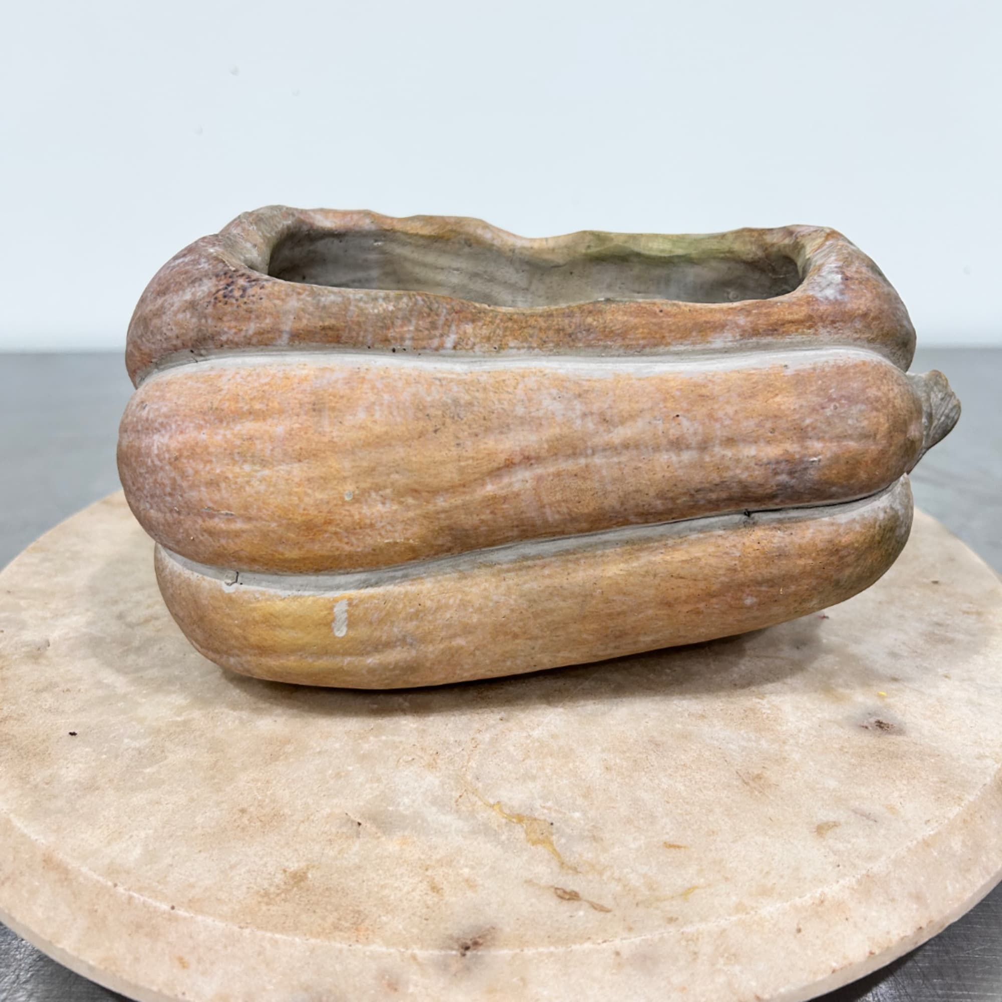 Empty pumpkin-shaped ceramic planter on a round stone base