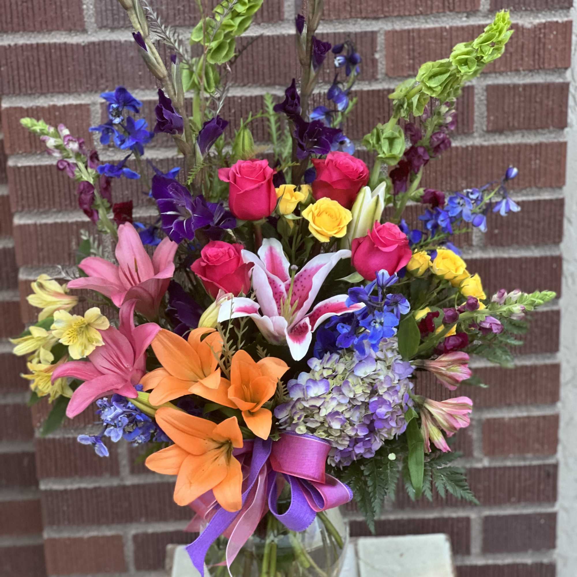 Colorful mixed bouquet in a glass vase with lilies, roses, and hydrangea