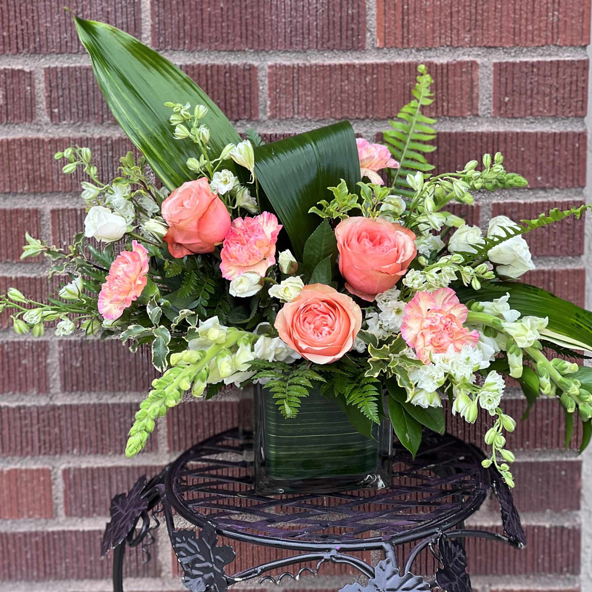 Coral roses and white flowers in a glass vase with broad leaves