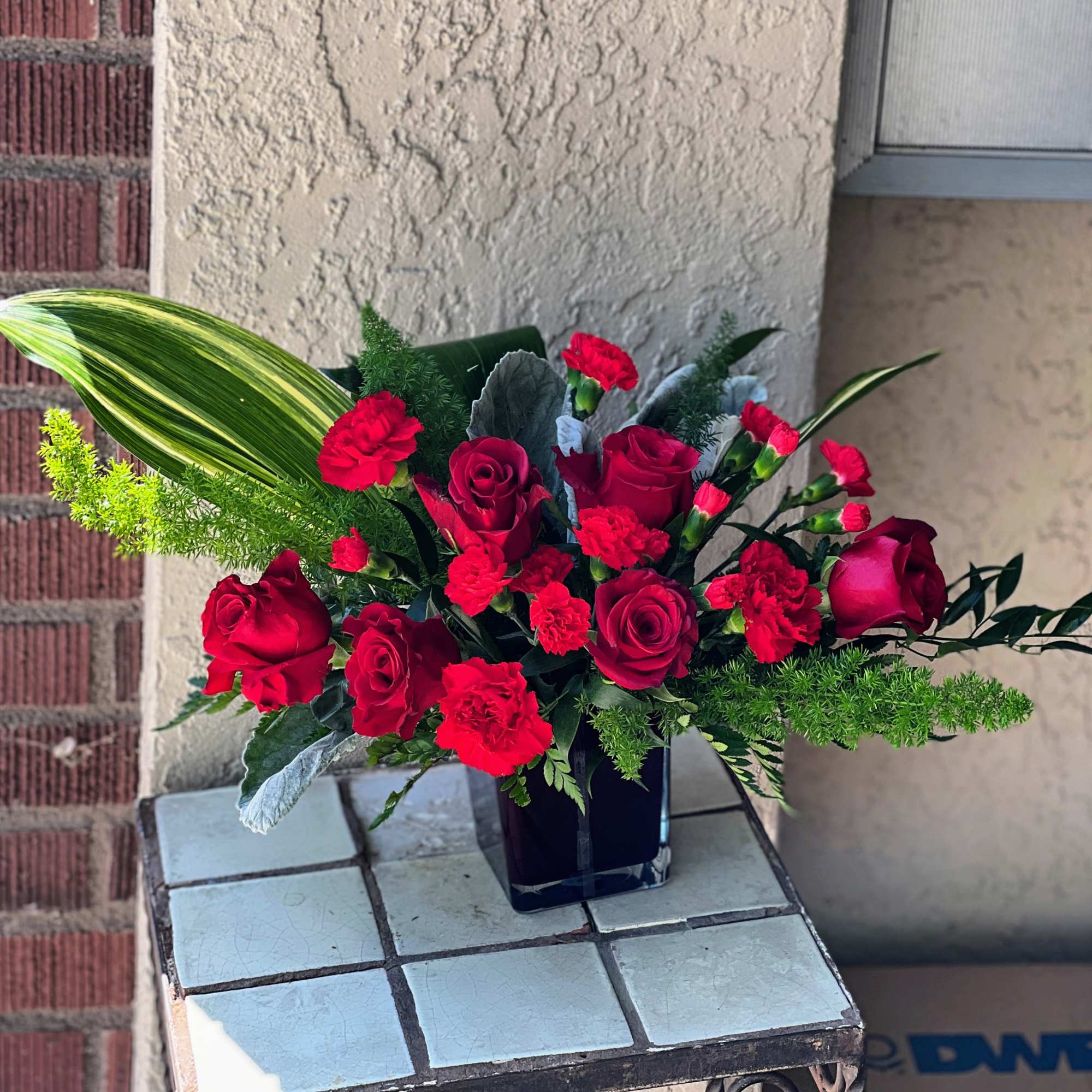 Red roses and carnations in a black vase with green foliage