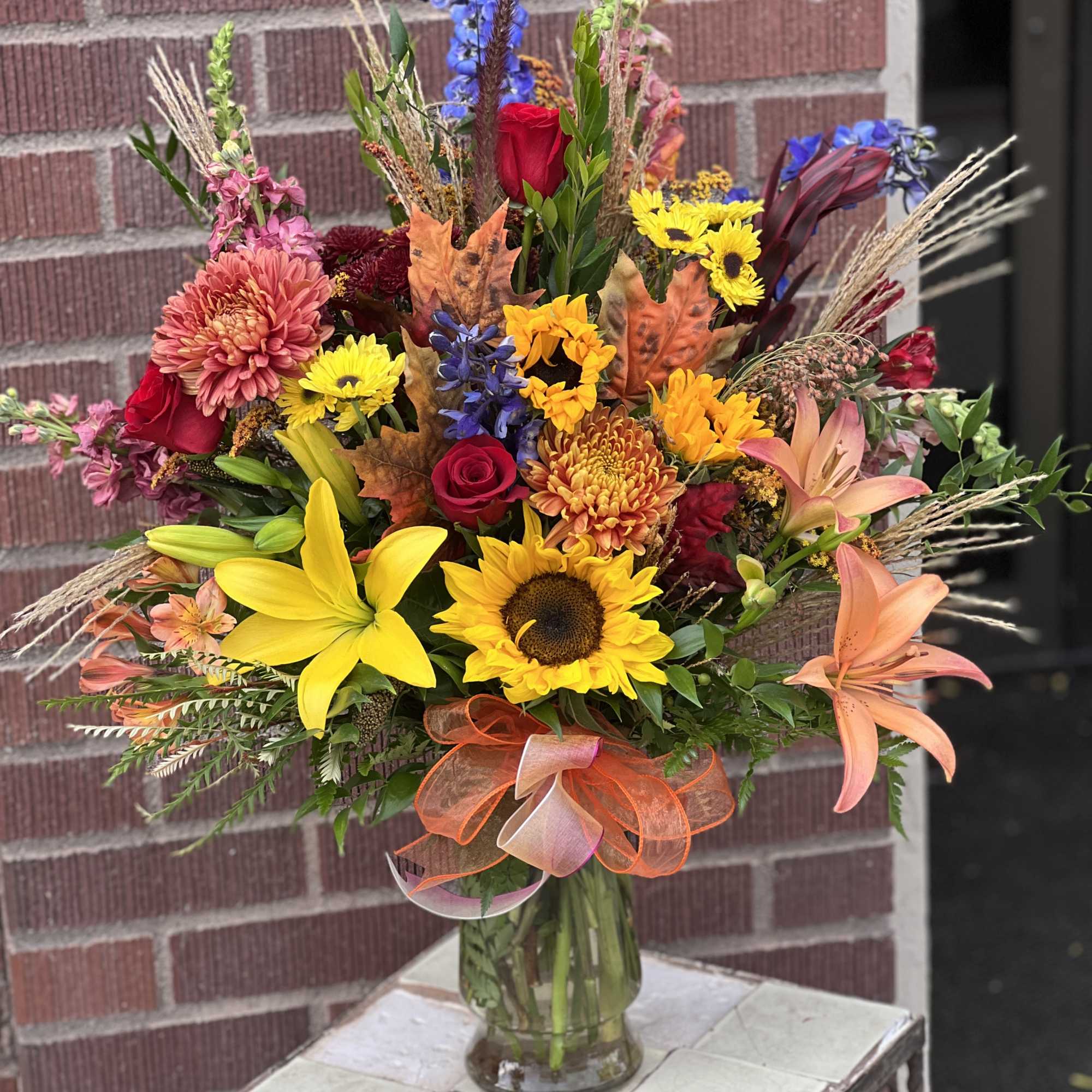 Mixed bouquet in a glass vase with sunflowers, roses, lilies, and autumn leaves
