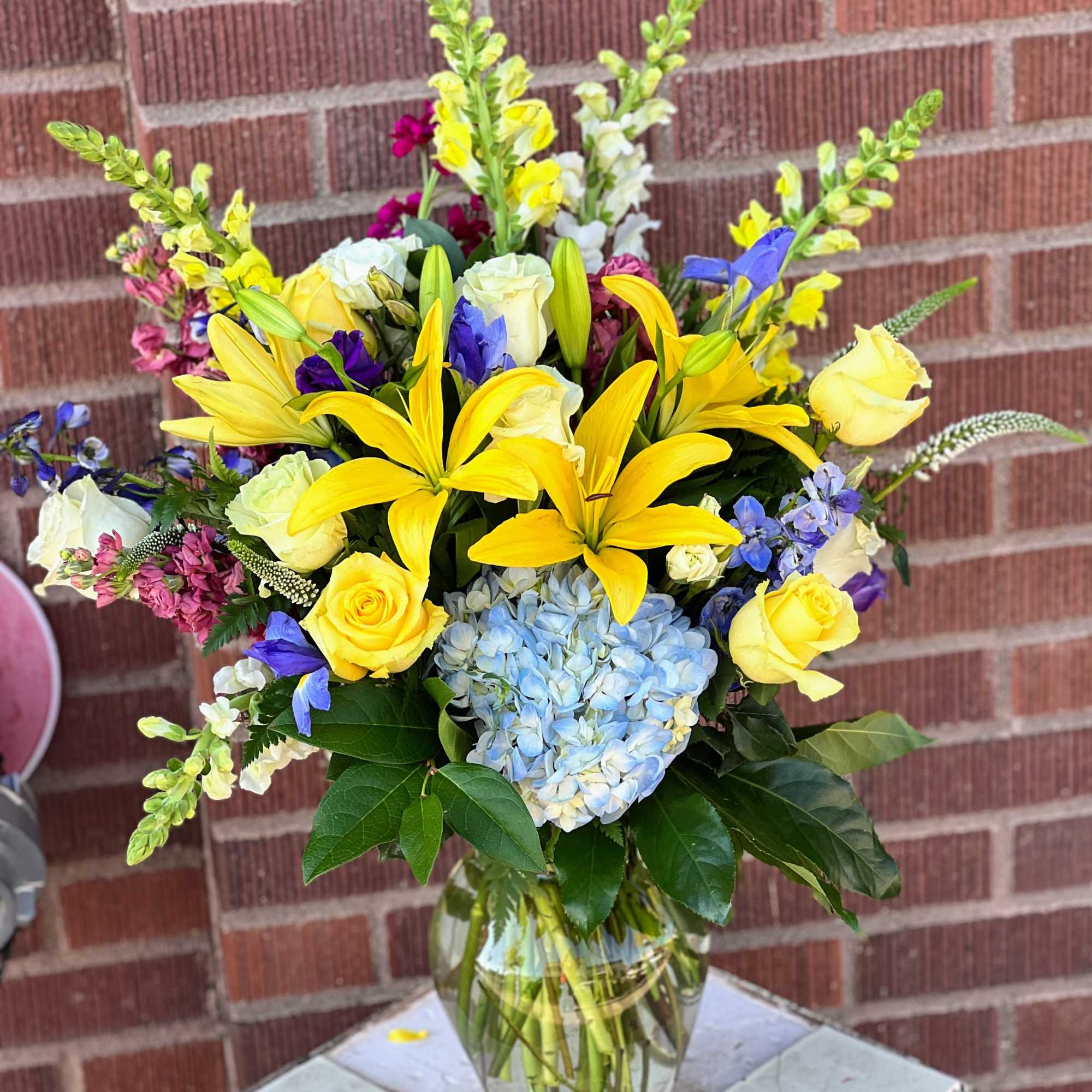 Bouquet of yellow lilies, roses, and blue hydrangea in a glass vase
