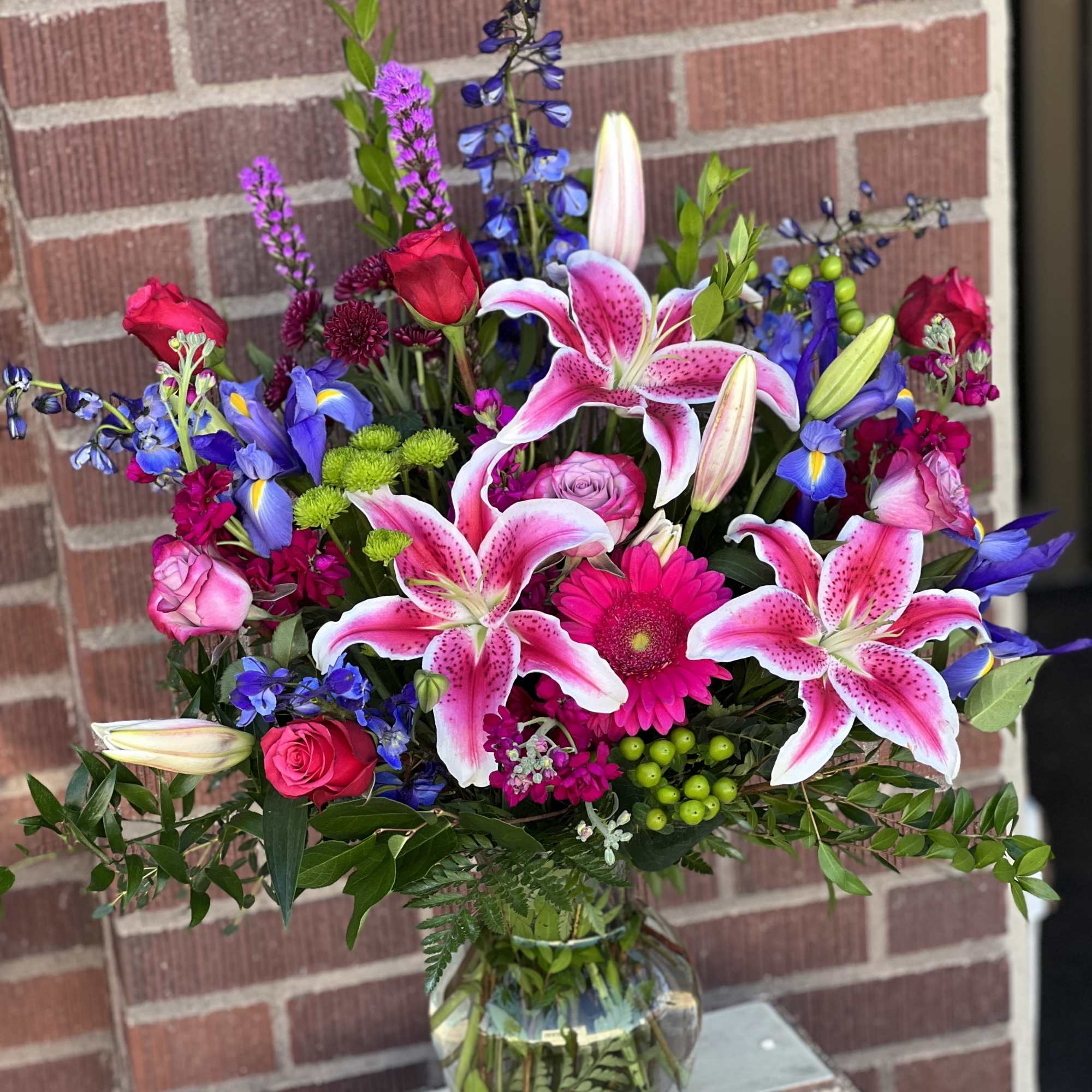 Mixed bouquet with pink lilies, roses, and blue flowers in a glass vase