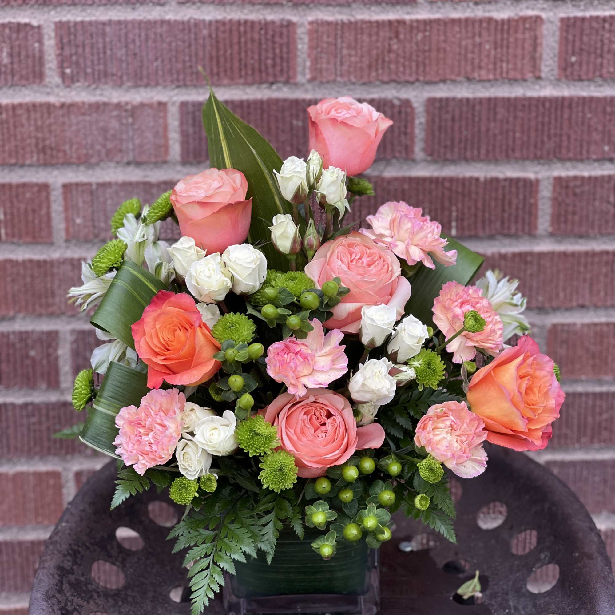 Pink and coral roses with white and green accents in a square vase