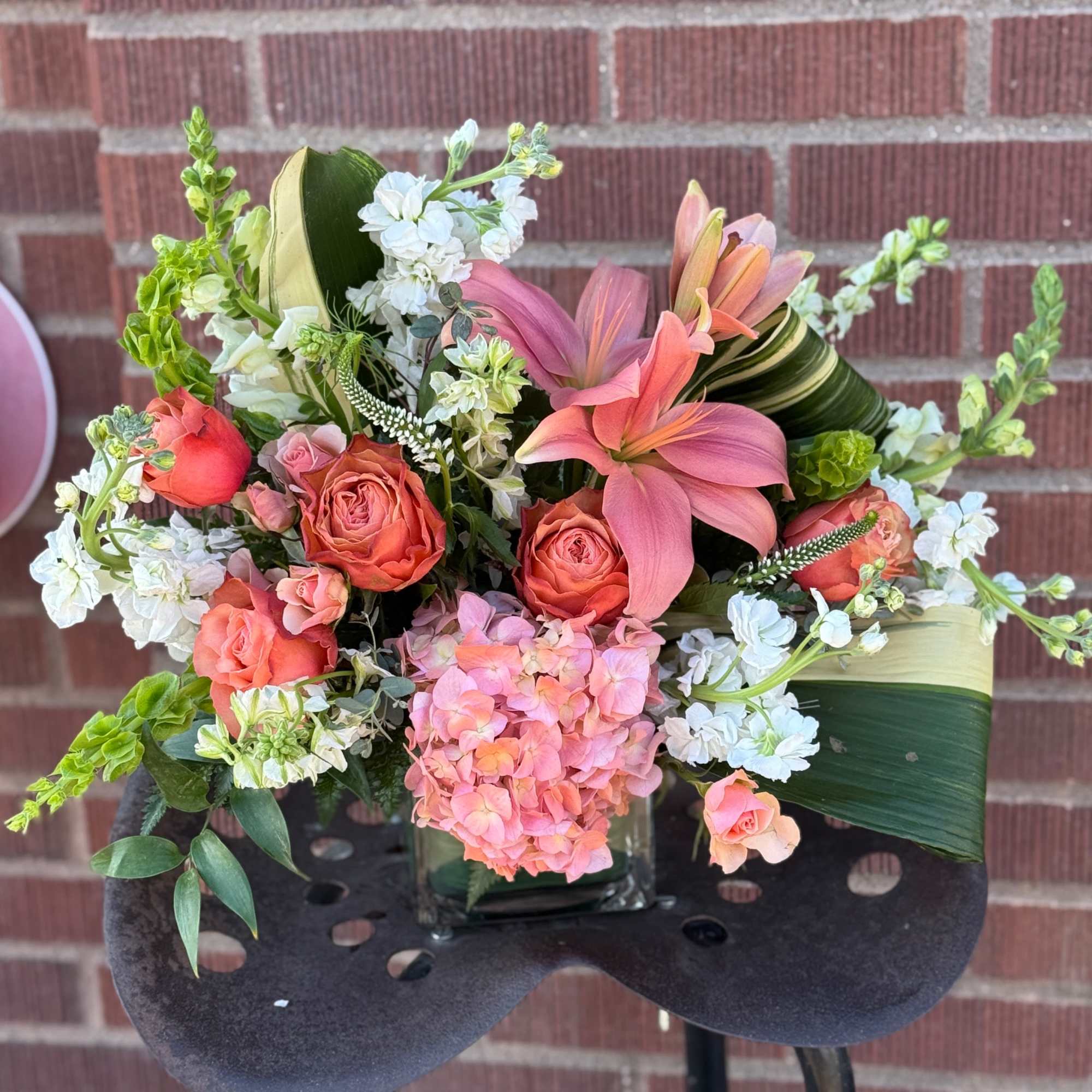 Pink lilies and coral roses arranged in a square glass vase