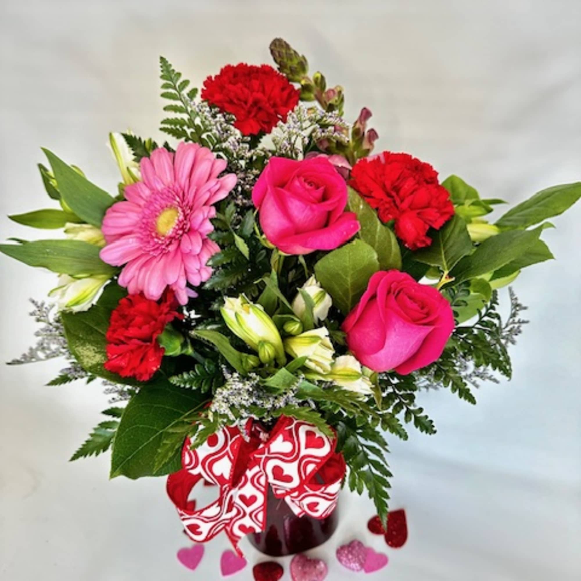 Pink roses and carnations in a vase with a heart ribbon