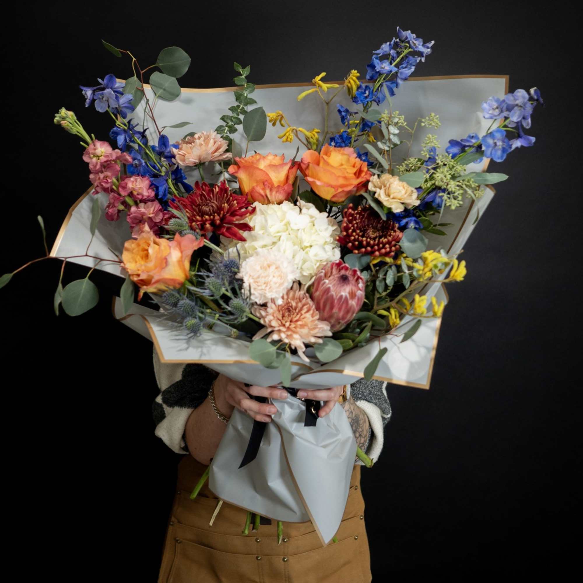 Large mixed bouquet with orange roses, blue flowers, and protea