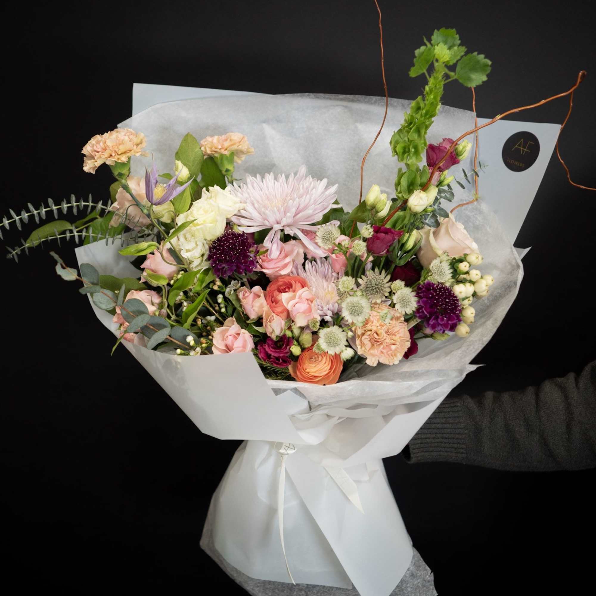 Mixed bouquet of pink, peach, and white flowers wrapped in white paper