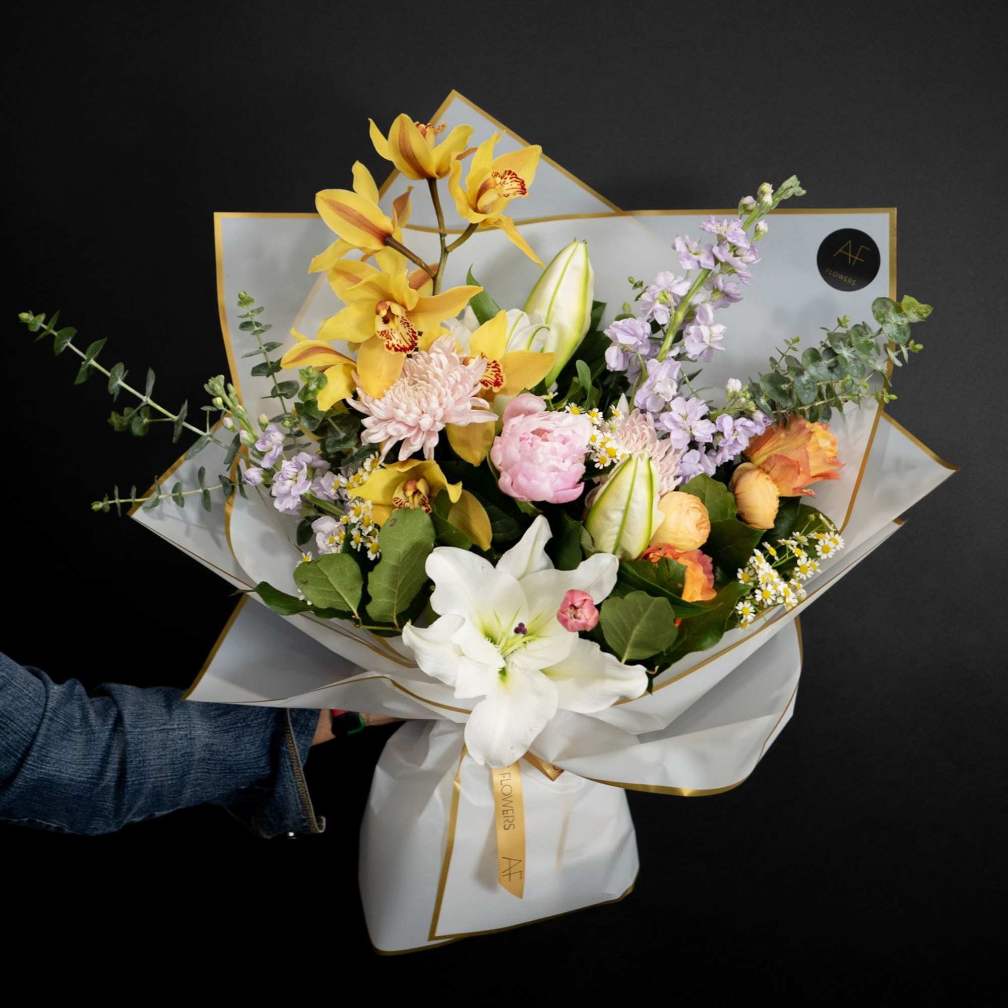 Bouquet of yellow orchids, white lilies, and pink flowers wrapped in white paper