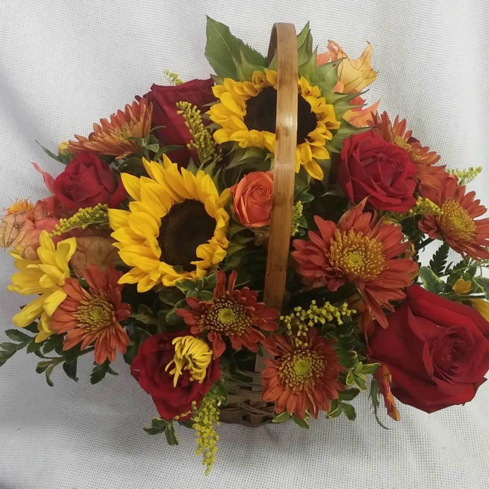 Basket arrangement with sunflowers, red roses, and orange mums