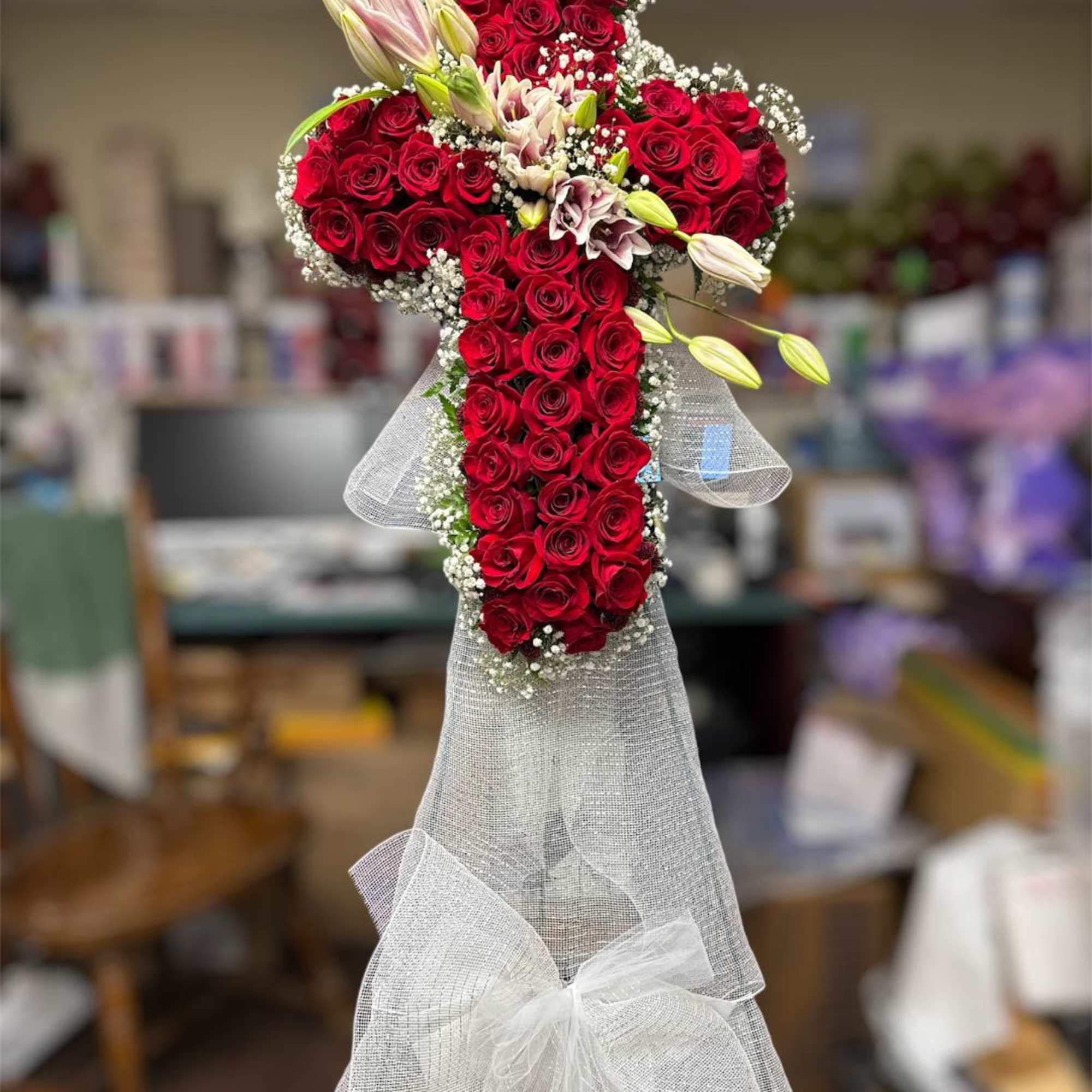 Cross-shaped arrangement of red roses with white lilies and sheer white ribbon