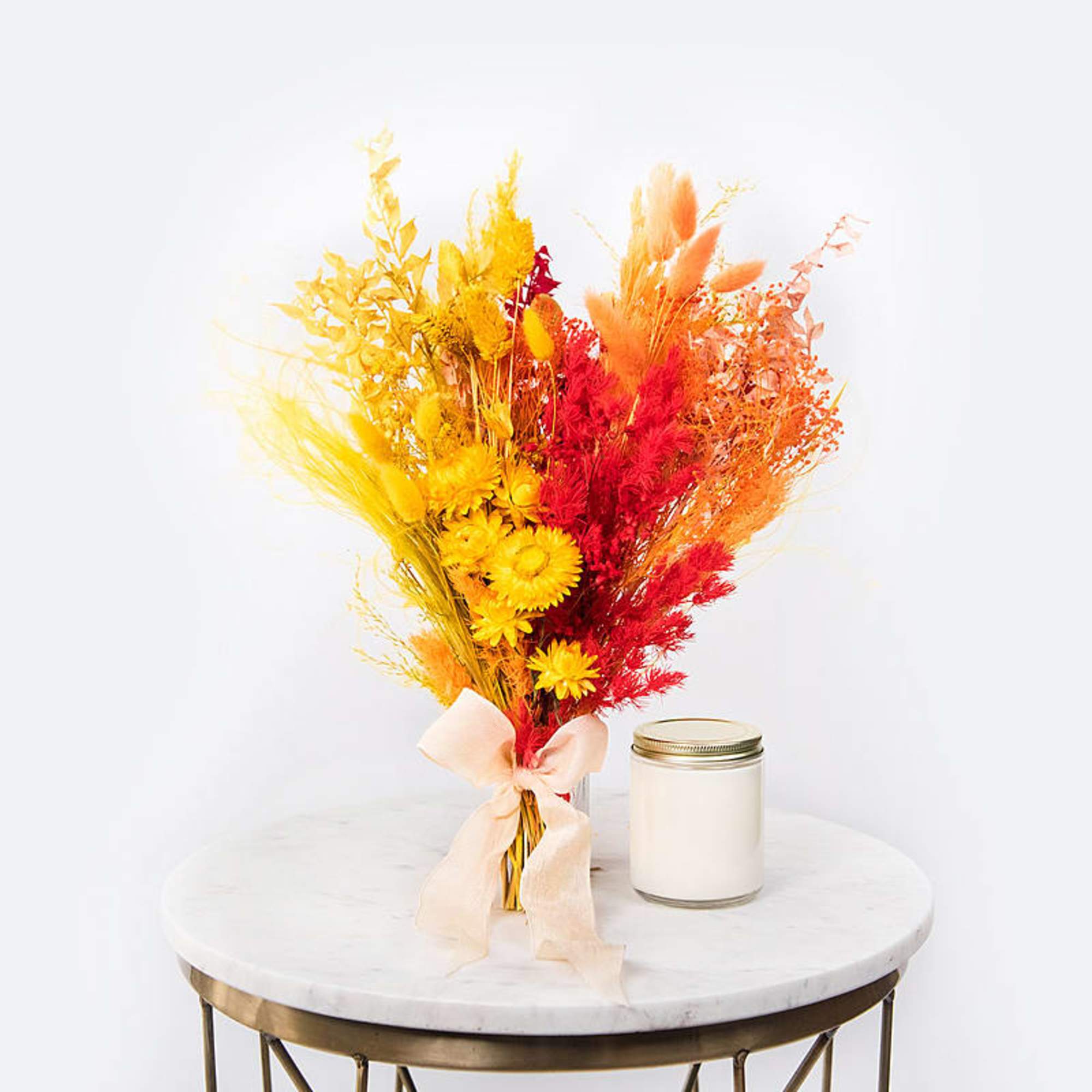 Bright dried flower bouquet with a pale ribbon beside a white candle jar
