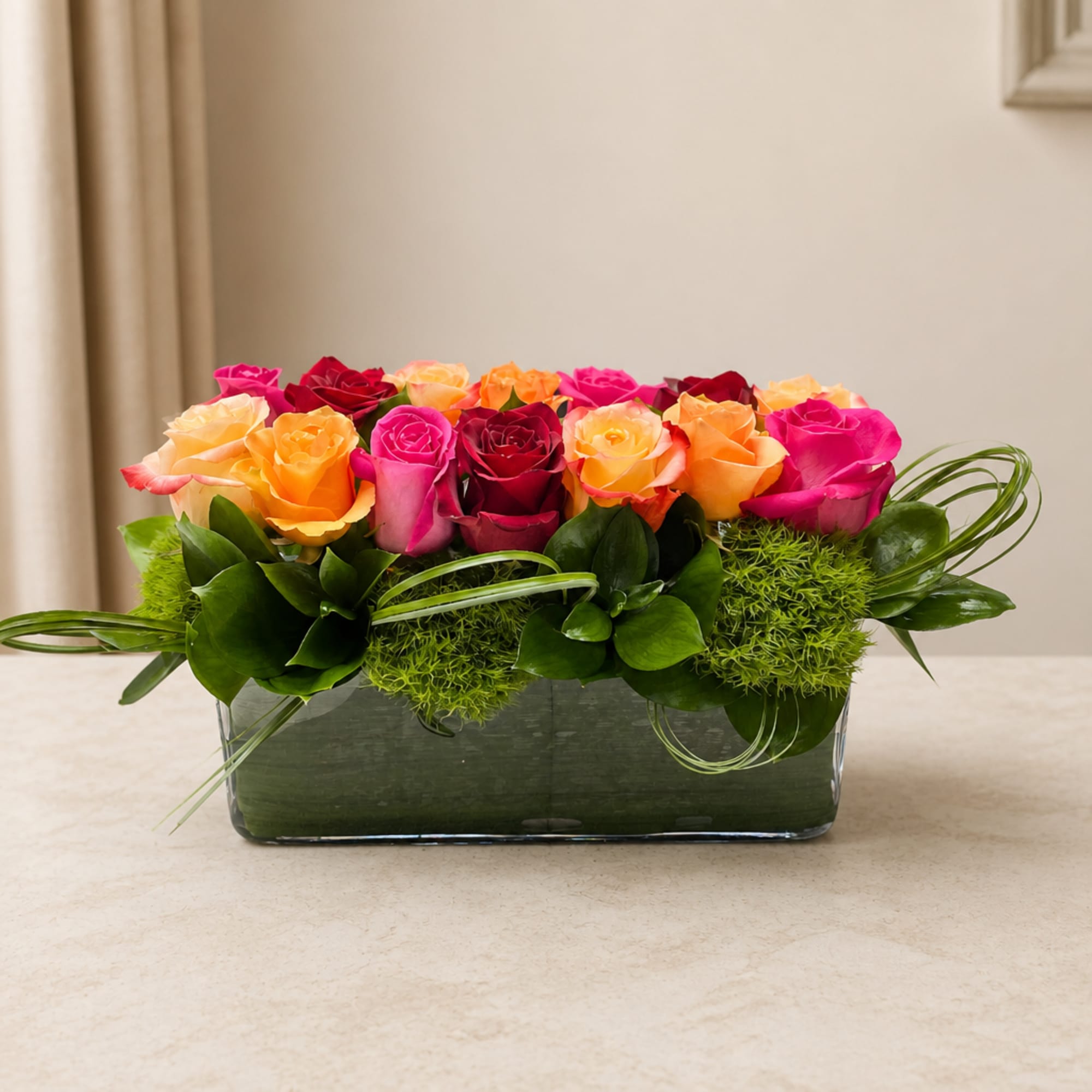Mixed roses in a low rectangular glass vase with green accents