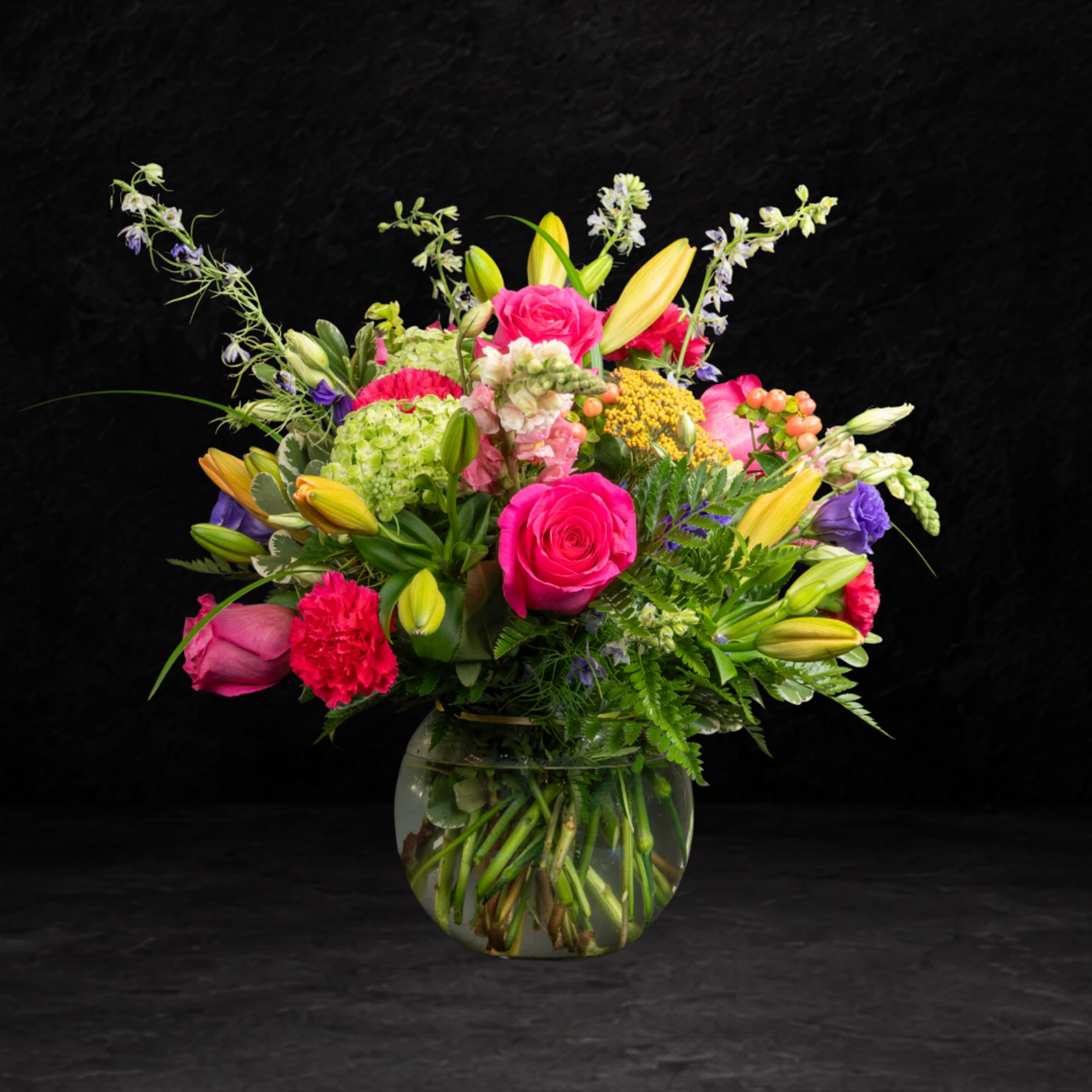 Bright mixed bouquet in a round glass vase with pink roses and yellow lilies