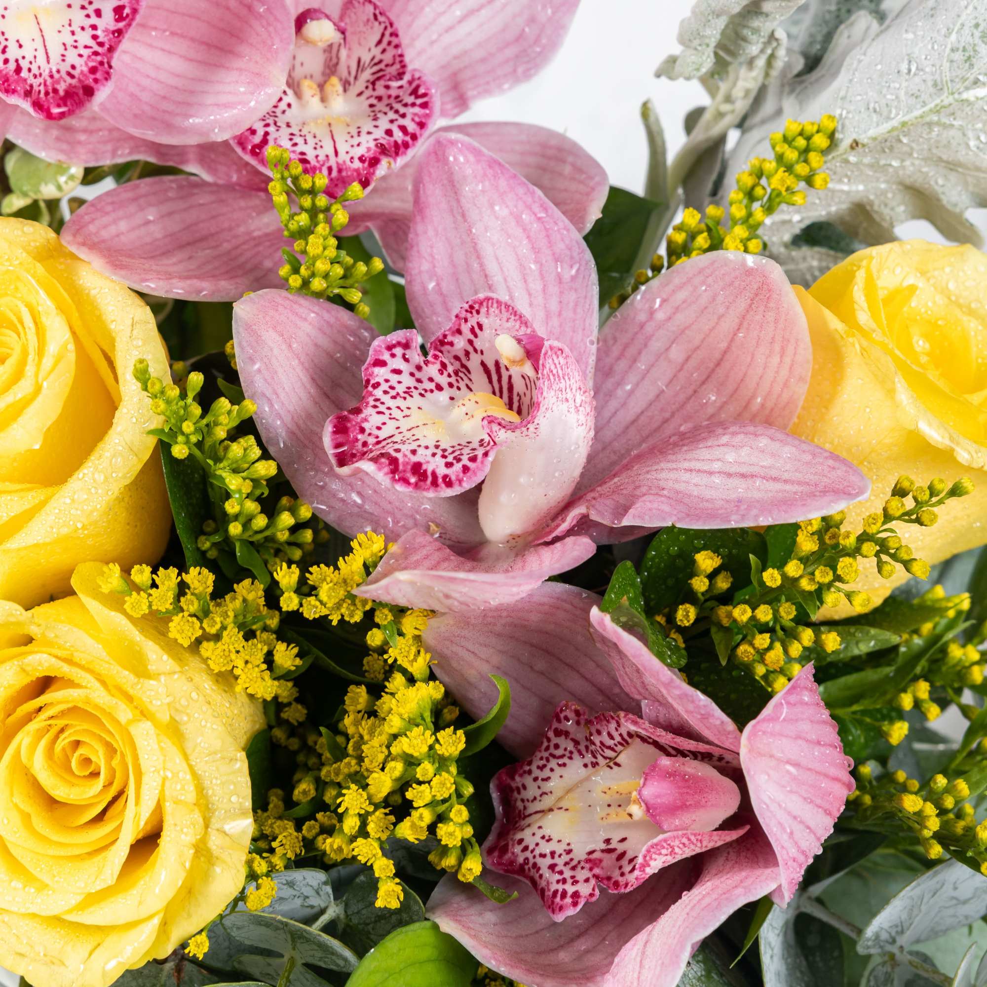 Close-up of an arrangement with yellow roses, pink cymbidium orchids, and small yellow filler flowers.