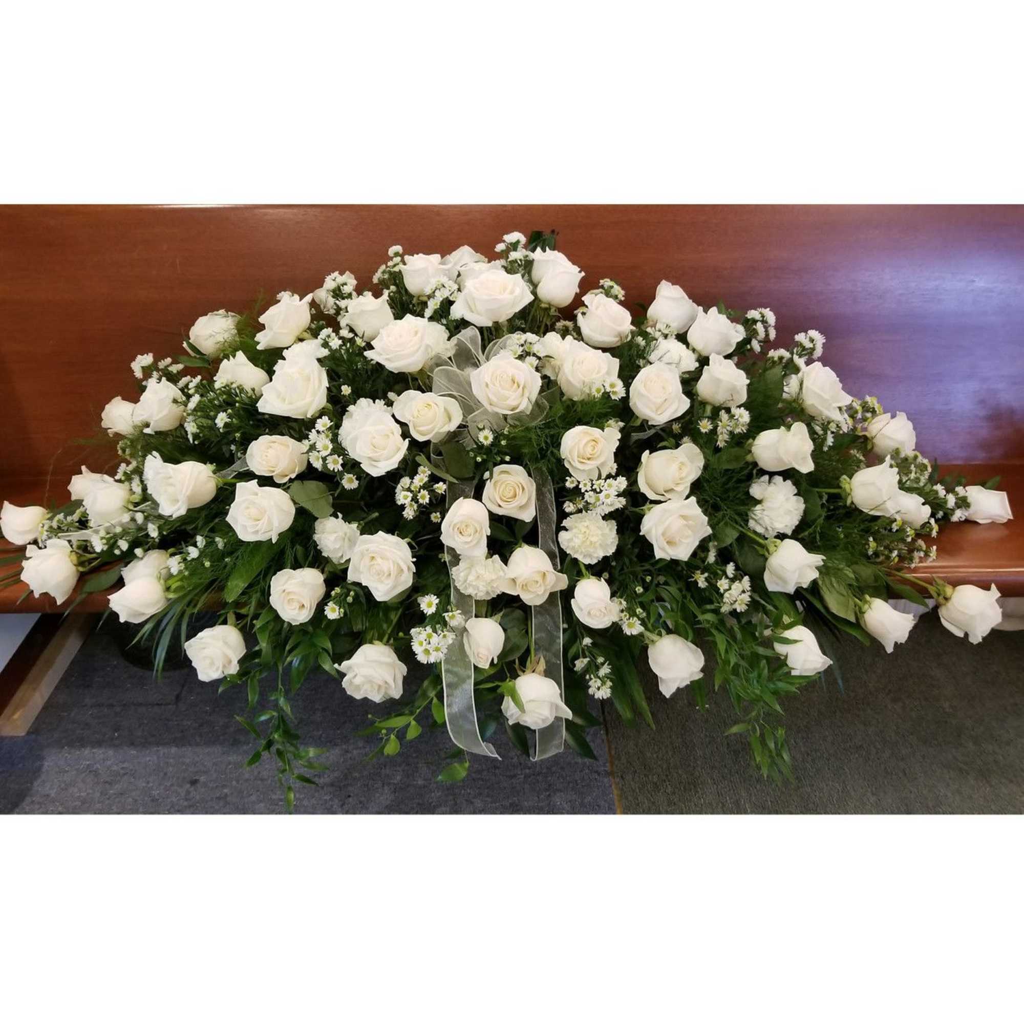 Large white rose casket spray with greenery and ribbon