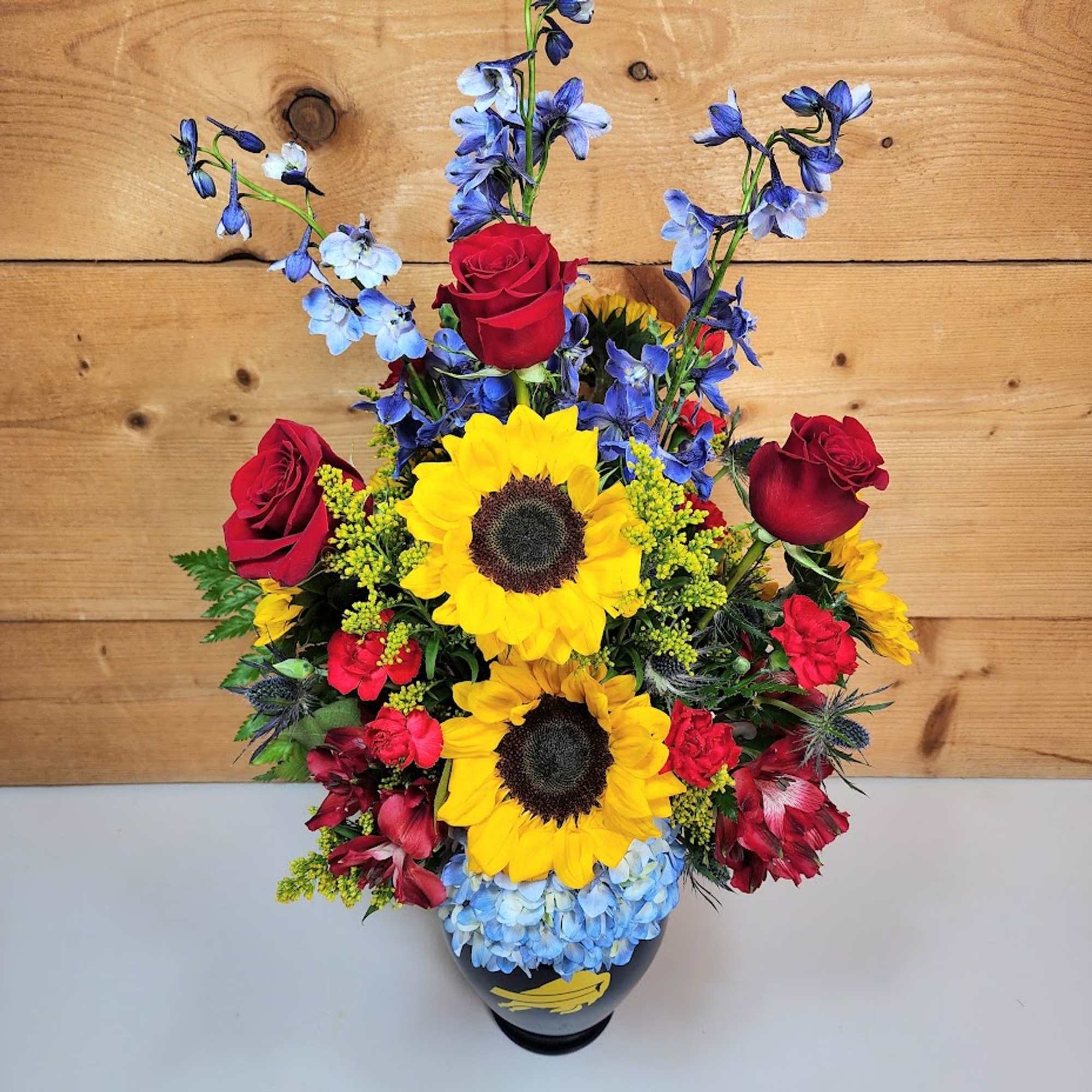 Bouquet of sunflowers, red roses, and blue flowers in a vase