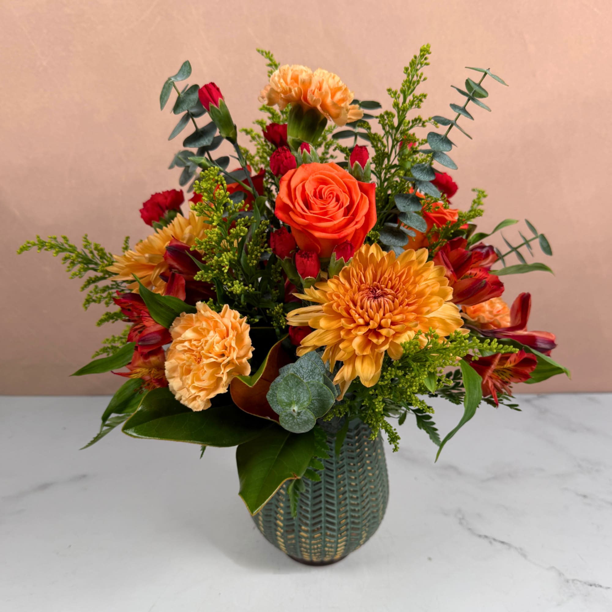 Mixed bouquet of orange, yellow, and red flowers in a textured vase