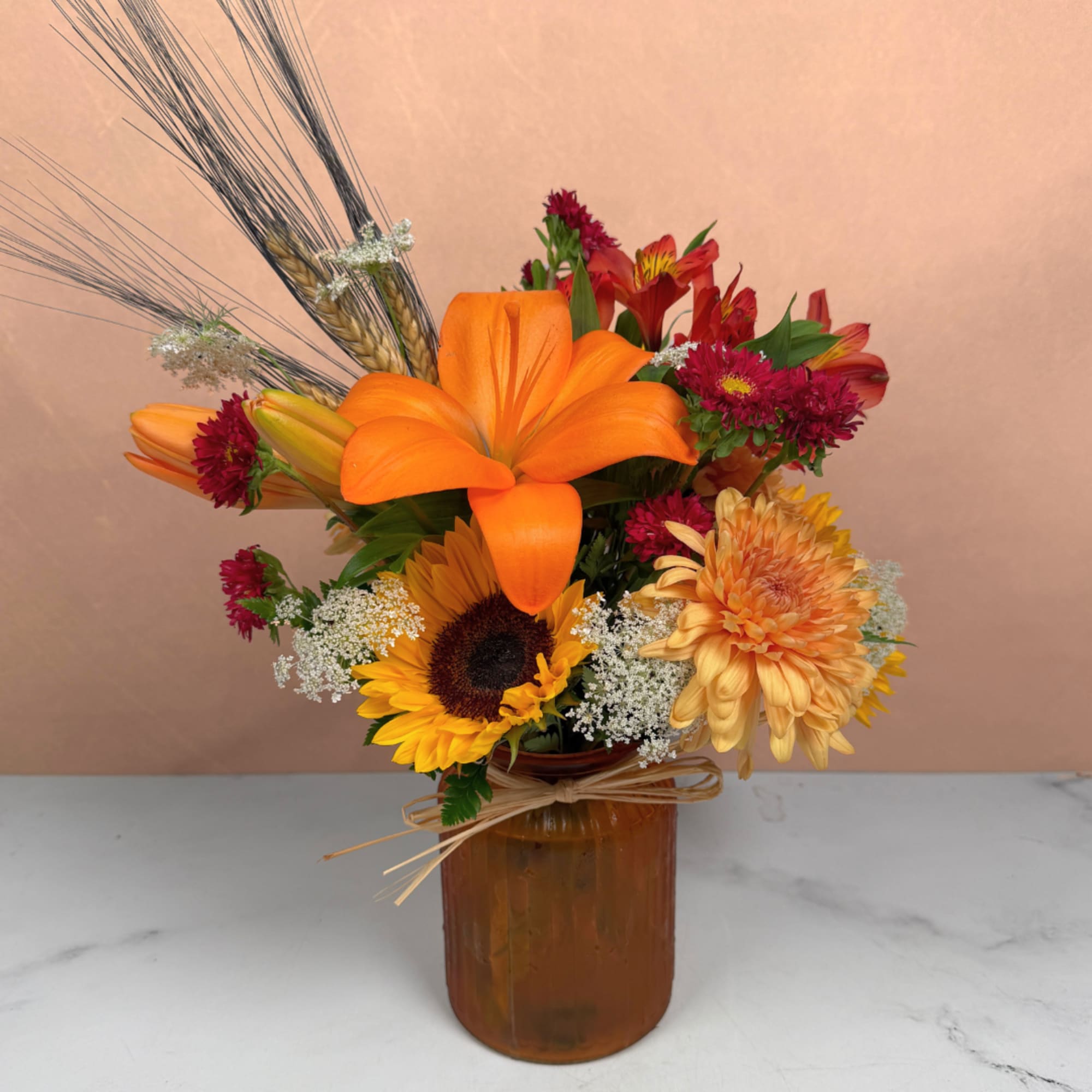 Mixed bouquet with orange lilies, sunflowers, and chrysanthemums in an amber vase