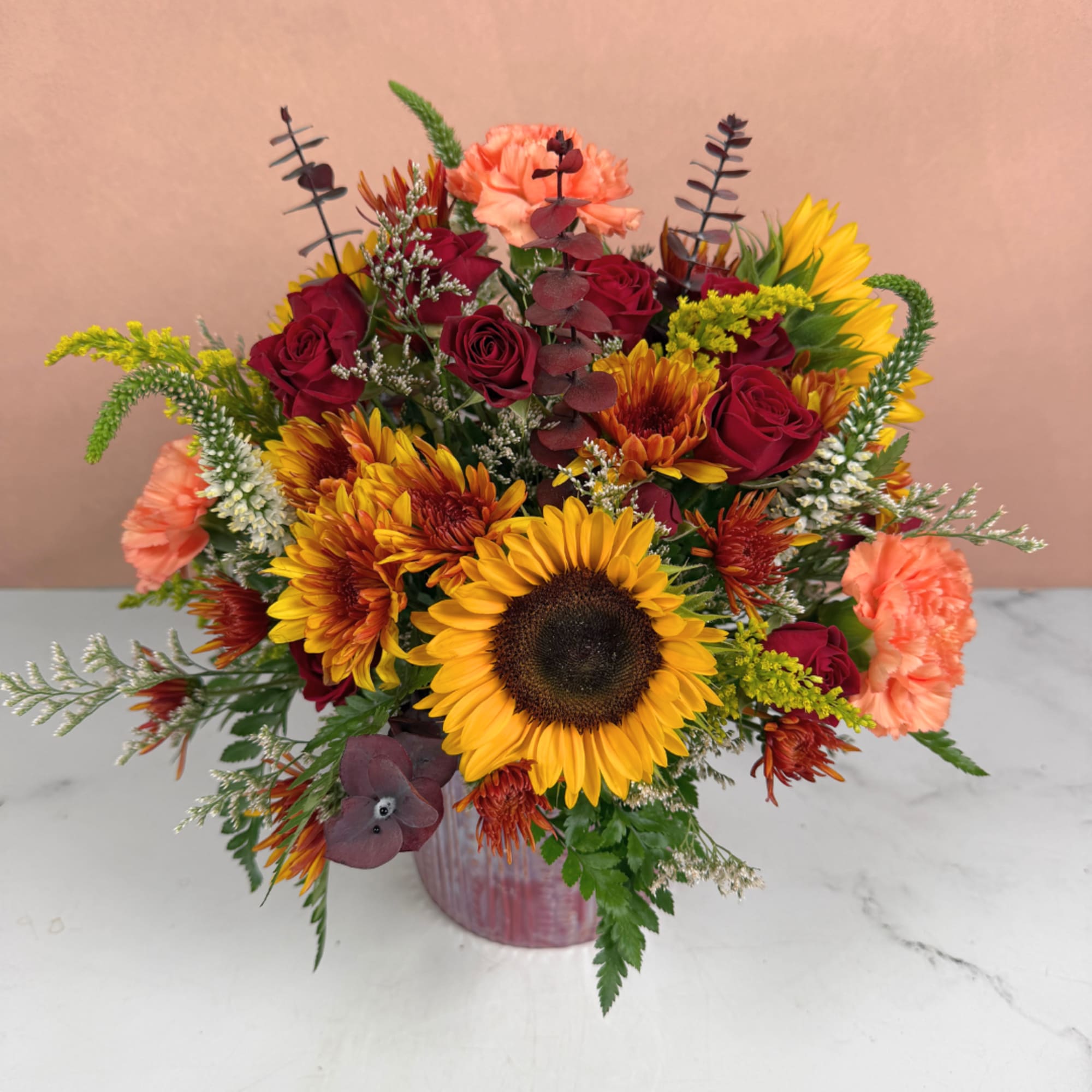 Mixed bouquet with sunflowers, red roses, and peach carnations in a vase